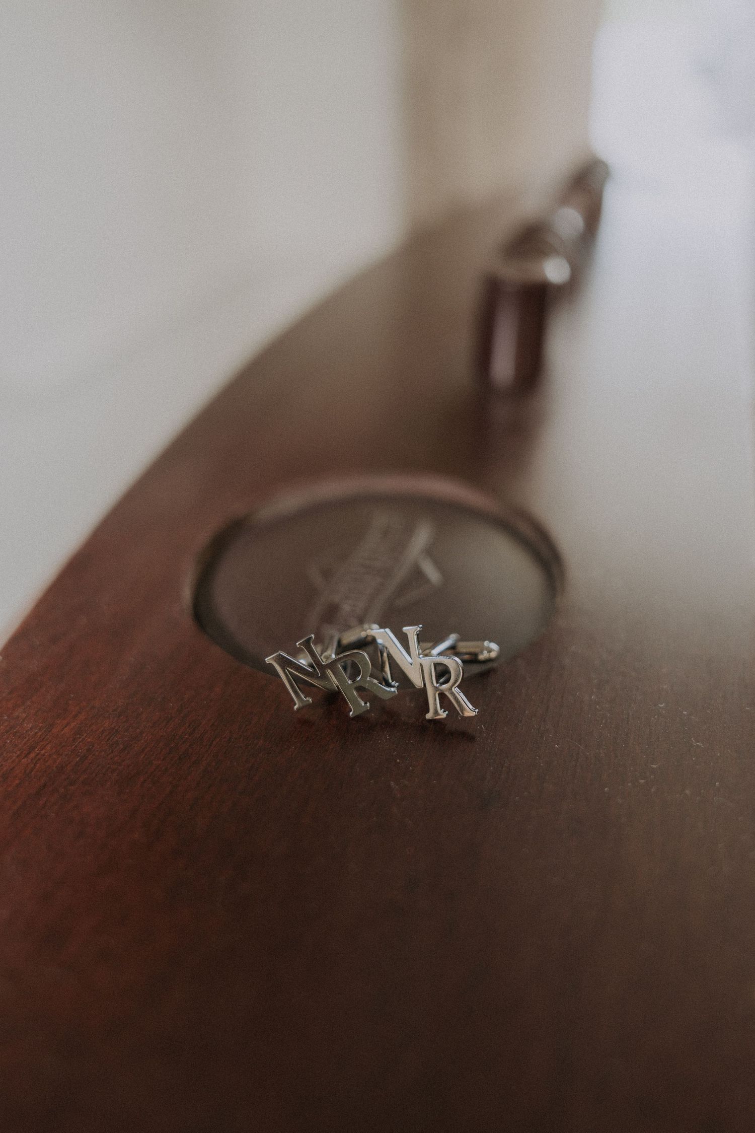Close-up of personalized silver monogram NR cufflinks resting on a wooden surface for a wedding day.