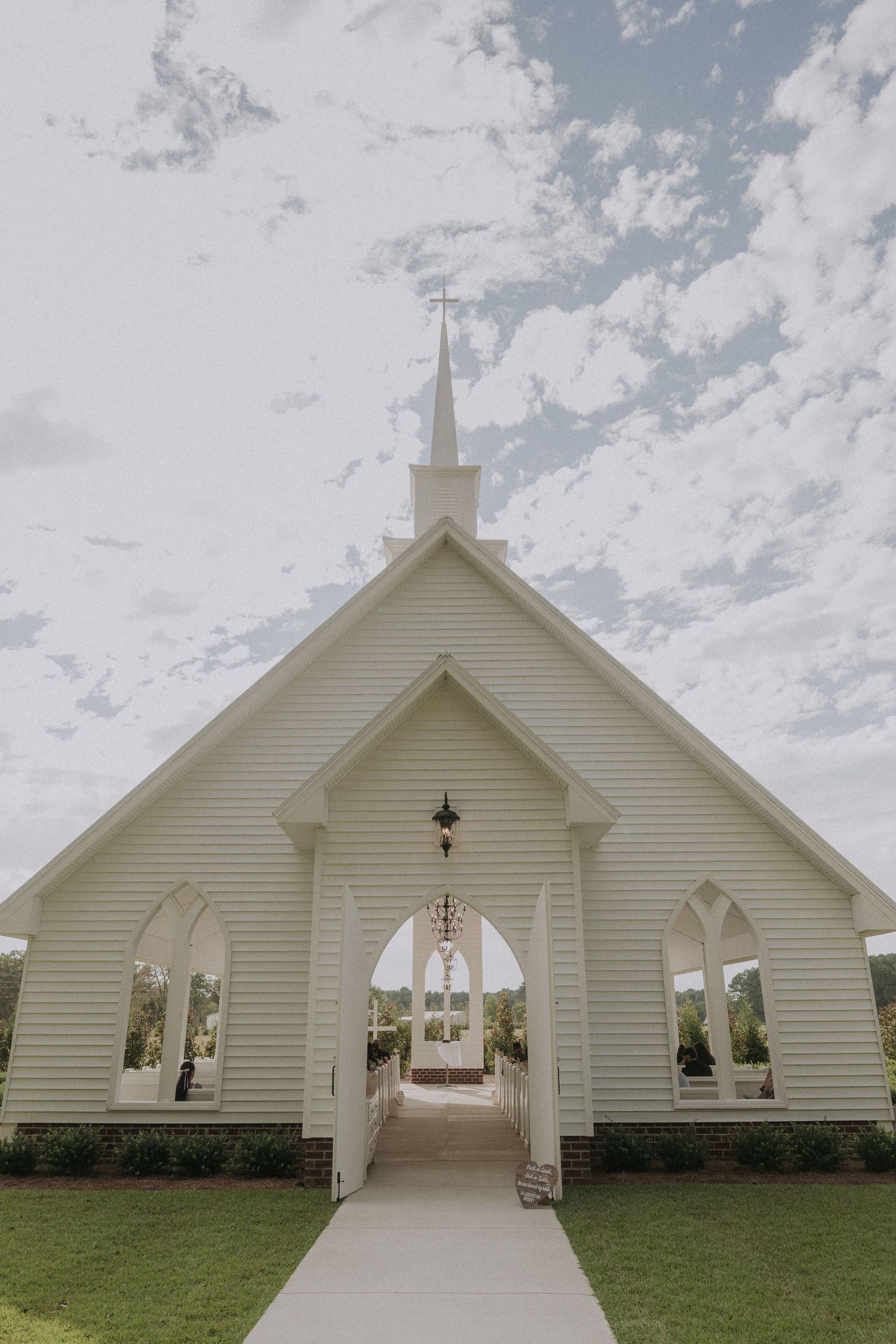 White chapel with steeple, arched entrance, and open gates under a partly cloudy sky.