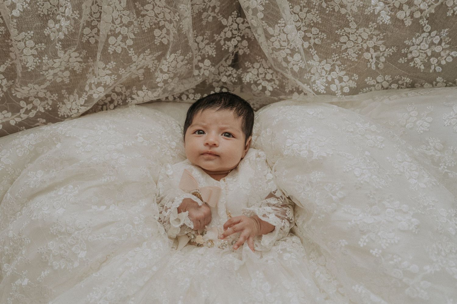 Baby wearing traditional white baptismal gown on textured background.