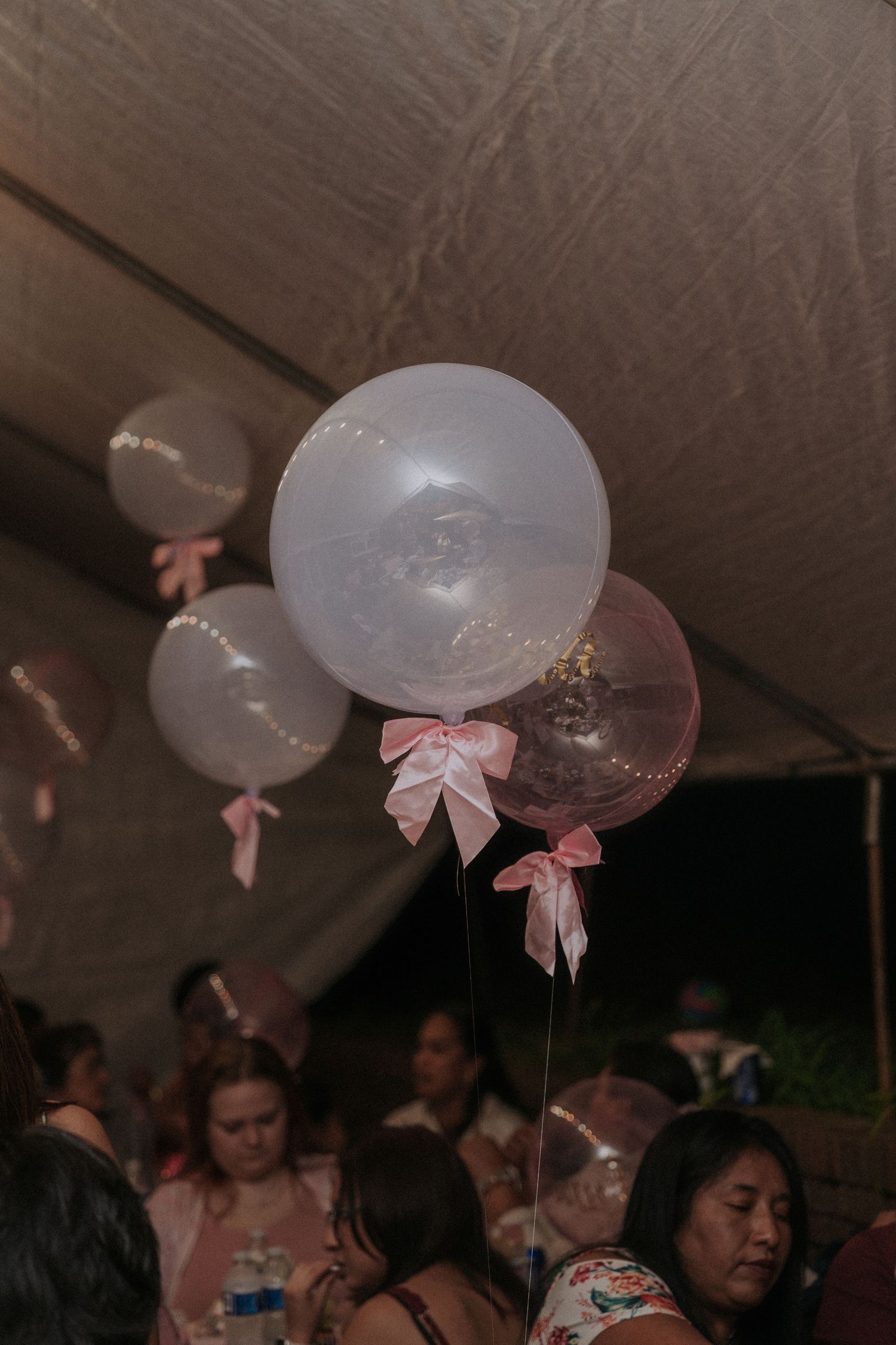 White balloons with pink bows decorating a dark ceiling at a celebration event.