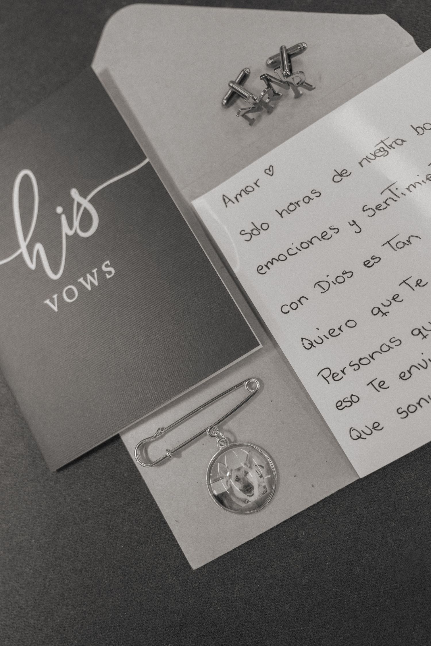 His vows card with handwritten Spanish love letter, cufflinks, and a photo brooch pin on gray background.