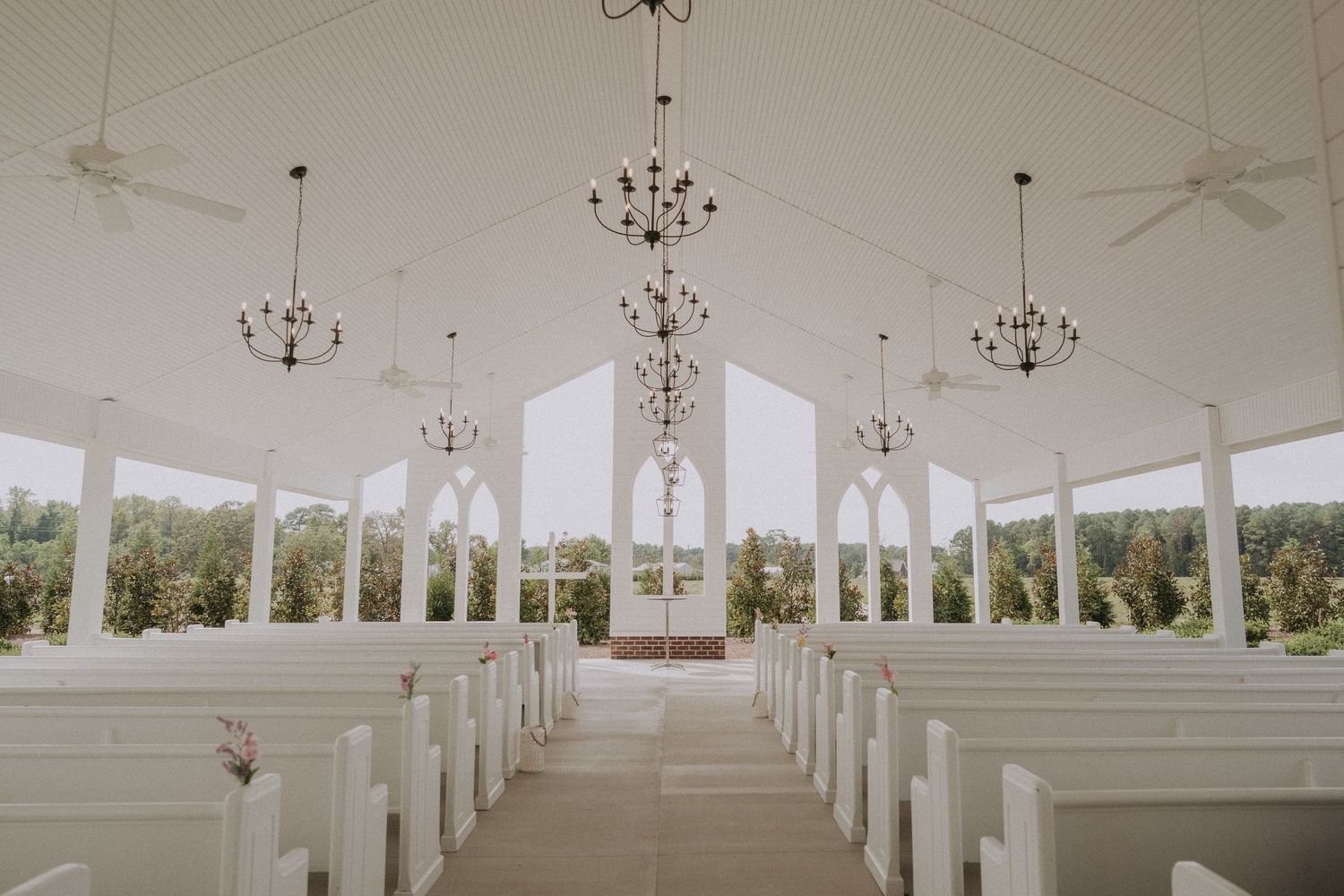Elegant all-white wedding chapel interior with chandeliers, white pews, and panoramic windows.