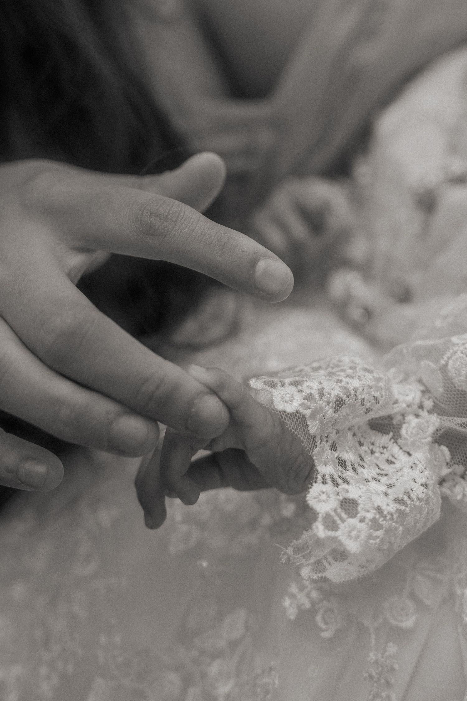 Close-up detail of baby hands and delicate white lace fabric with intricate floral patterns.