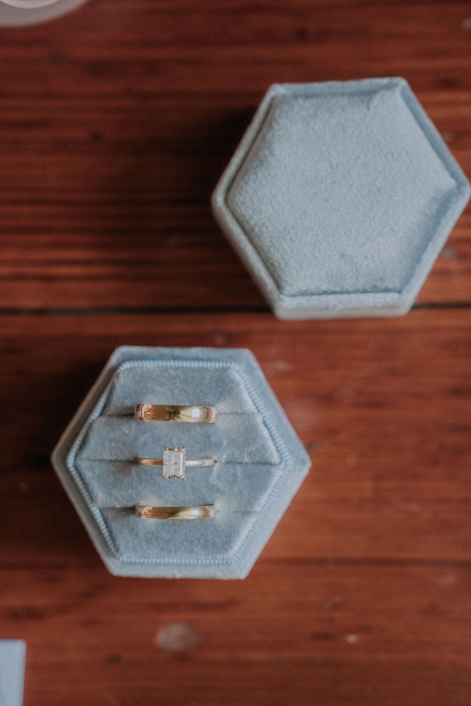 Three gold wedding rings displayed in open hexagonal blue velvet ring box on wood surface.