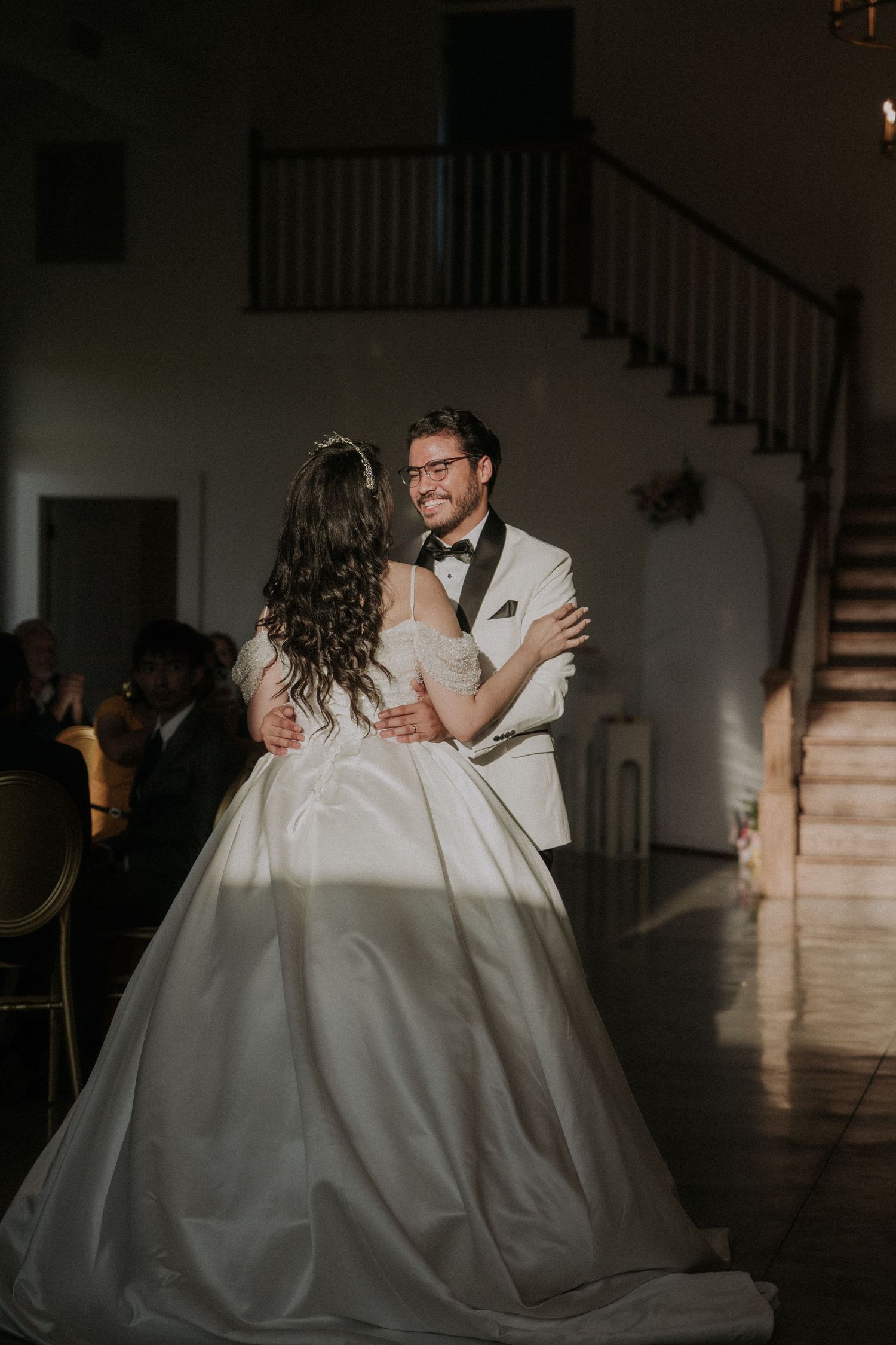 Groom in white tuxedo smiles at bride during their first dance in a stunning wedding reception venue.