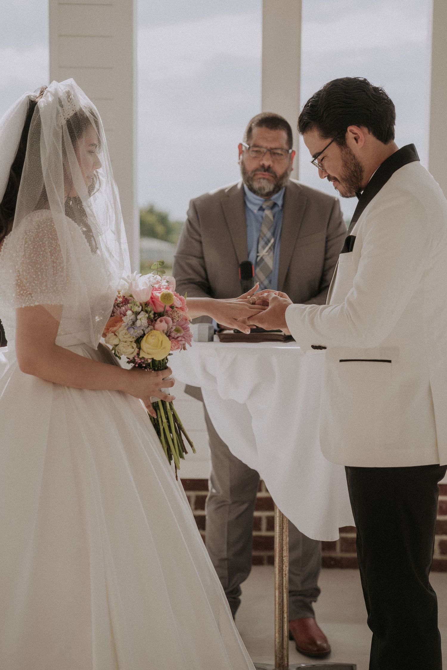 Groom places wedding ring on bride's finger while officiant watches during ceremony.