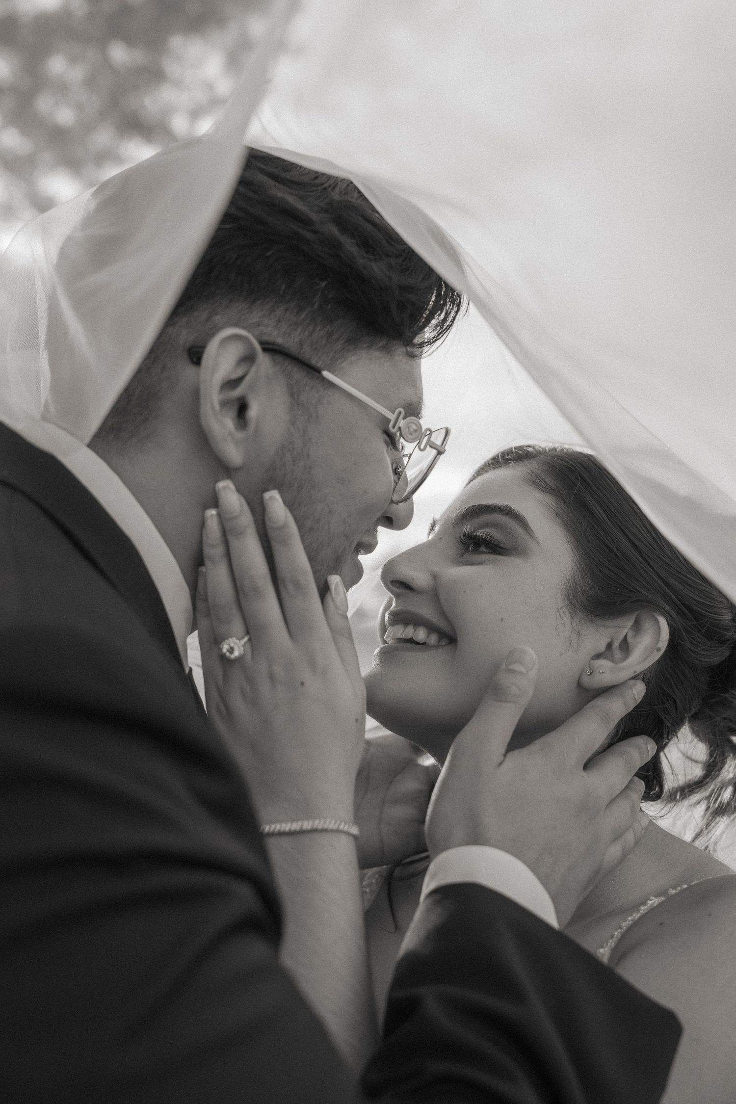 An intimate black and white portrait of a couple sharing a tender moment under a veil.