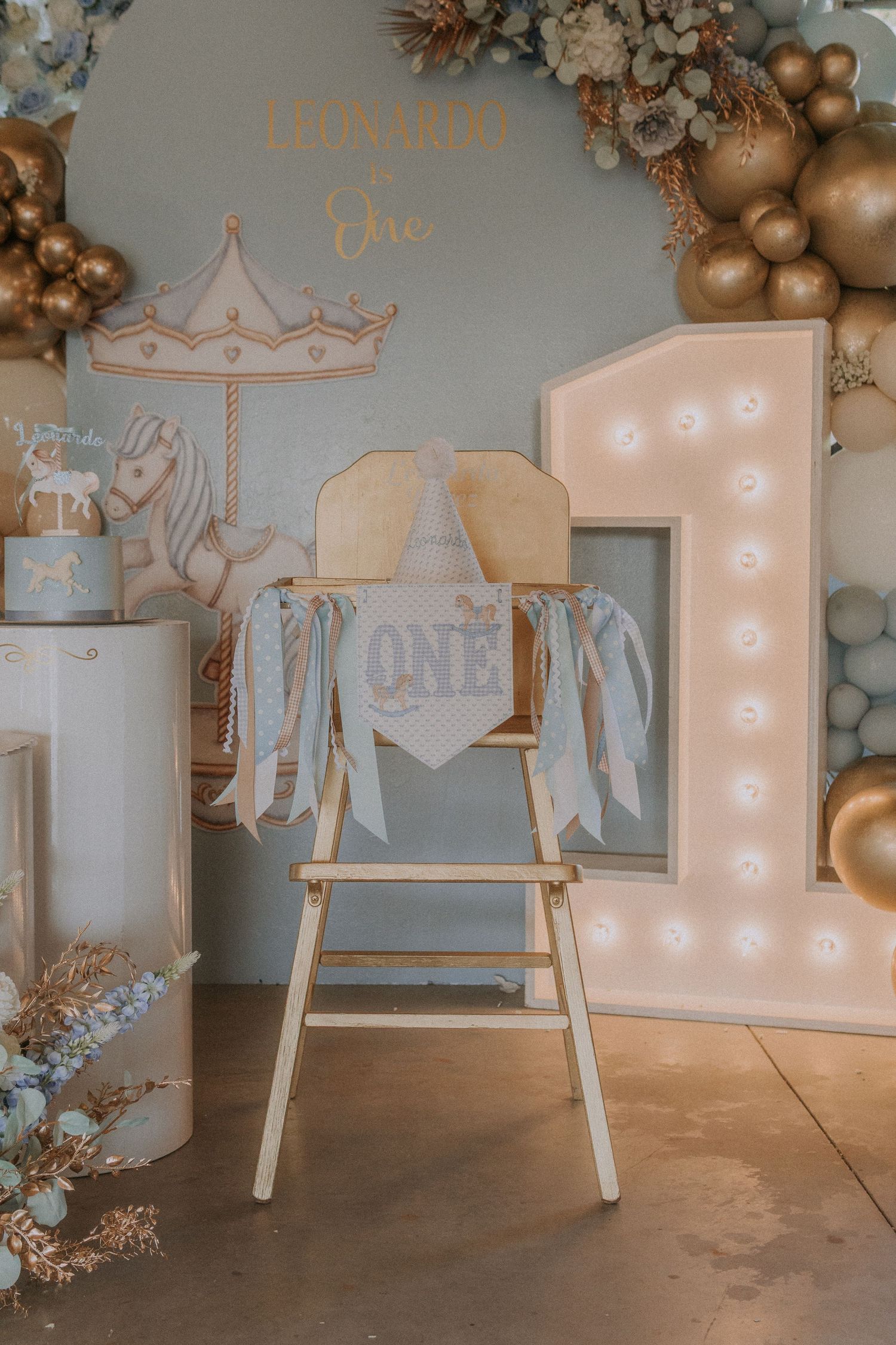 Modern first birthday decoration featuring carousel theme with balloon garland and illuminated display.