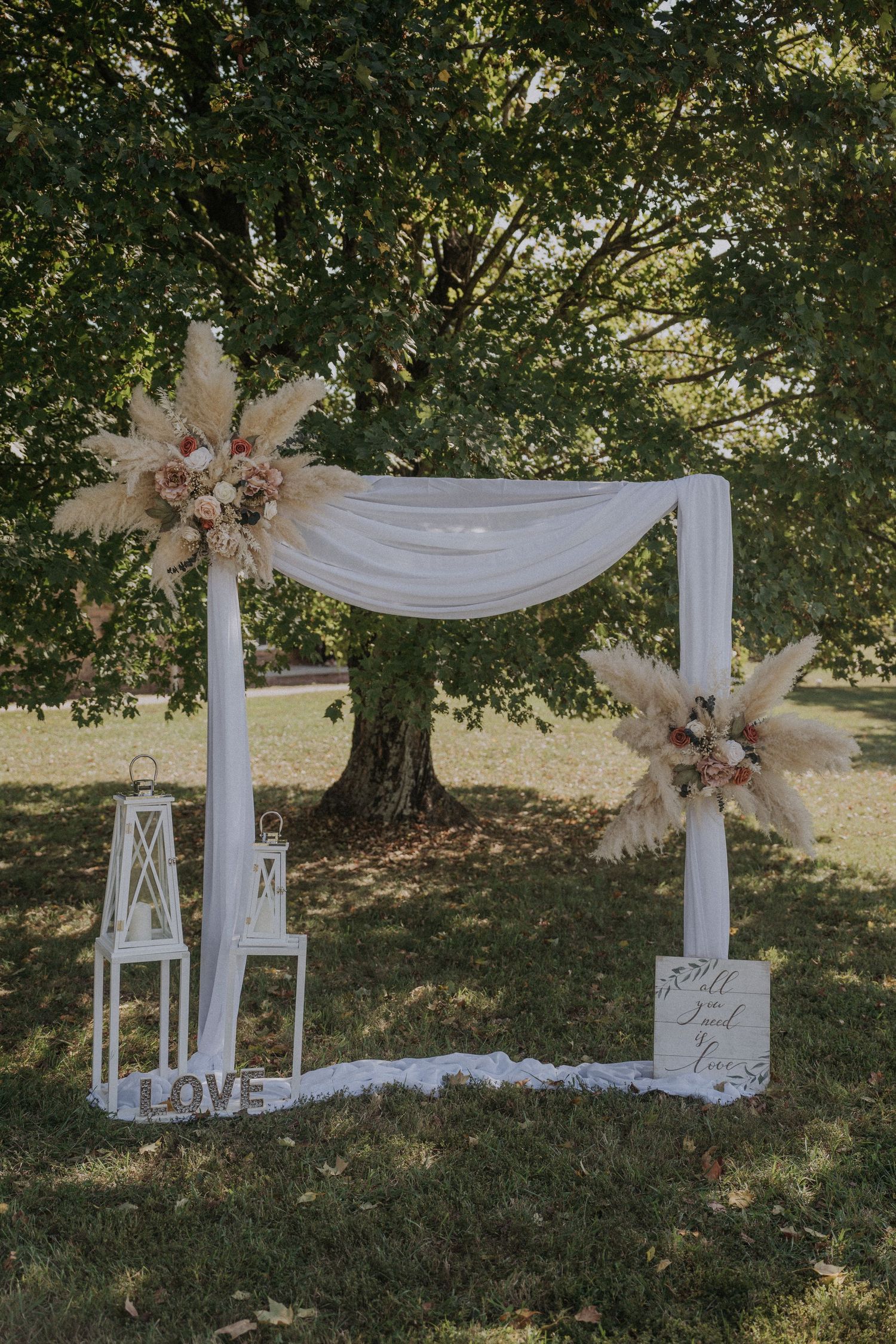 White draped wedding arch with lanterns and floral decorations set up in a scenic outdoor romantic setting.