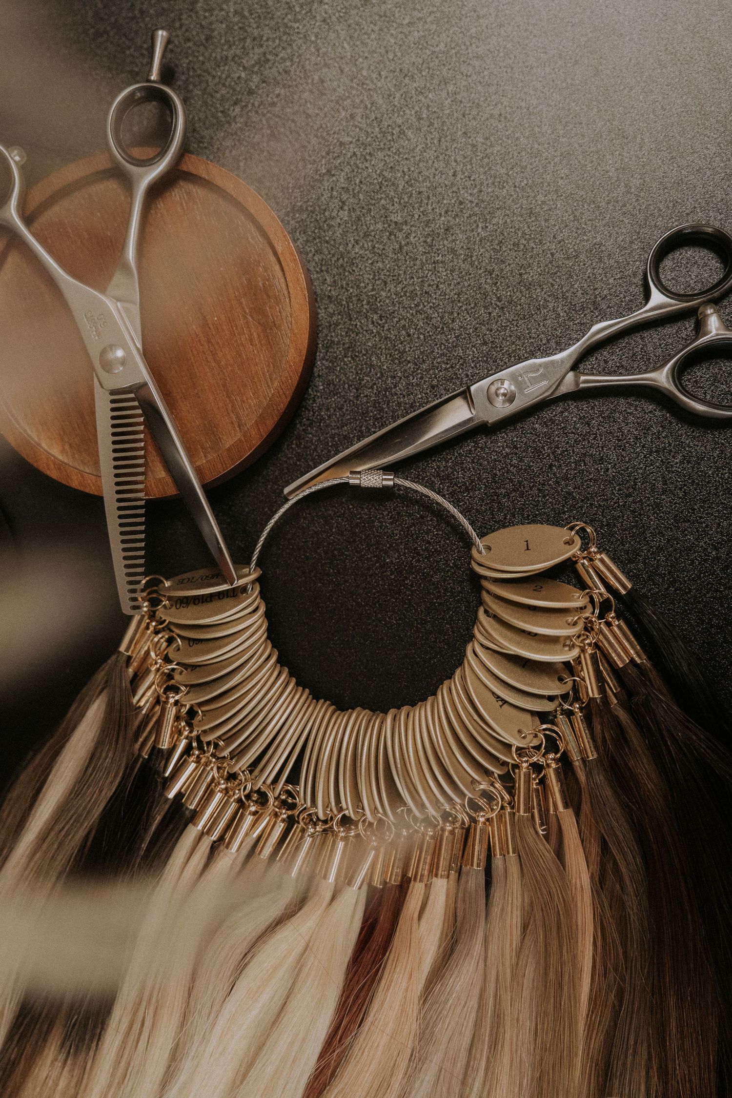 Close-up of hair extension tools and color swatches arranged on dark surface.