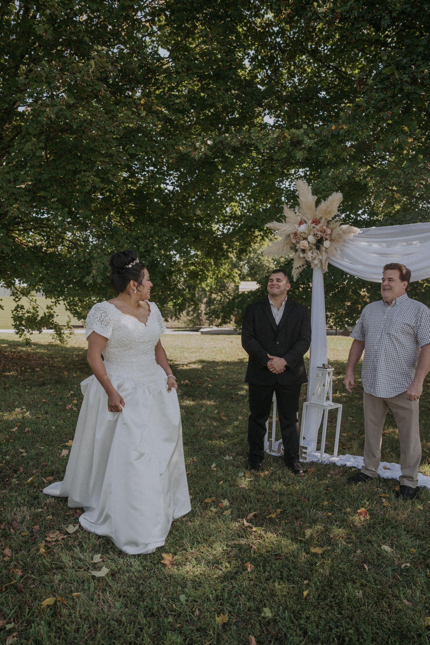 Outdoor vow renewal ceremony under trees with white decorations and formal attire.