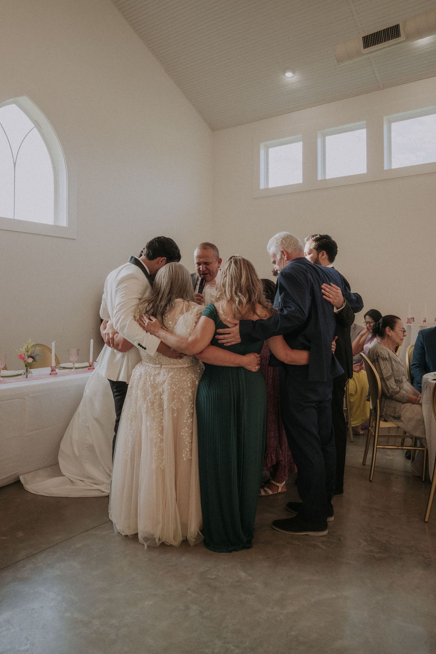 Wedding party sharing a group hug in a bright chapel venue during a joyful ceremony celebration.