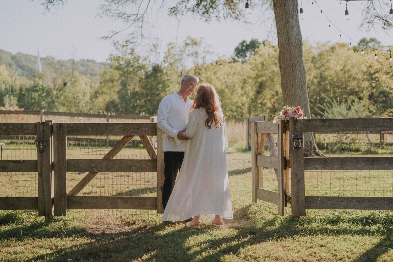 Romantic anniversary photos captured along a rustic wooden fence in countryside setting.