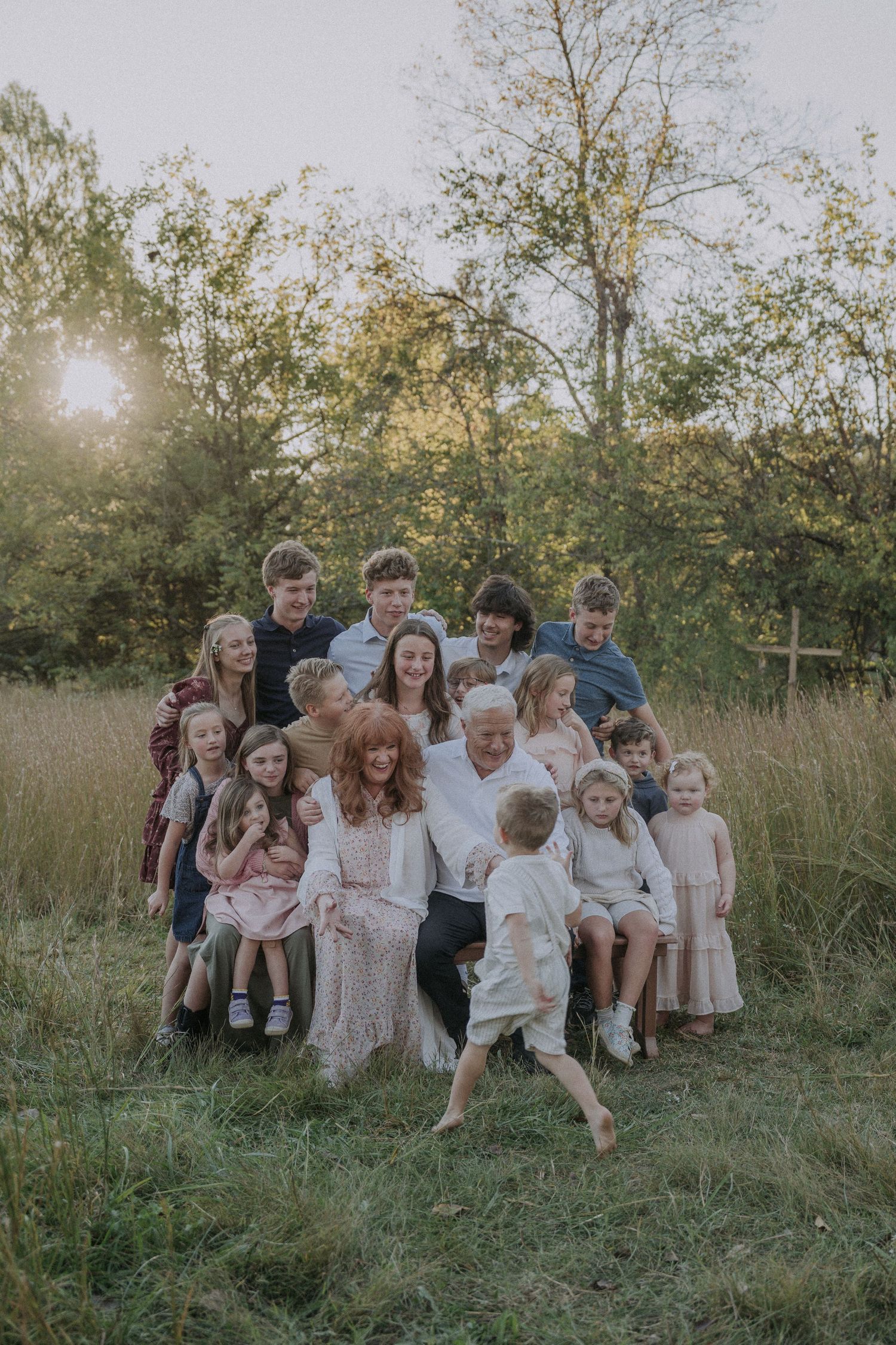 Large family gathered on a grassy hillside for a casual outdoor photo session at sunset.