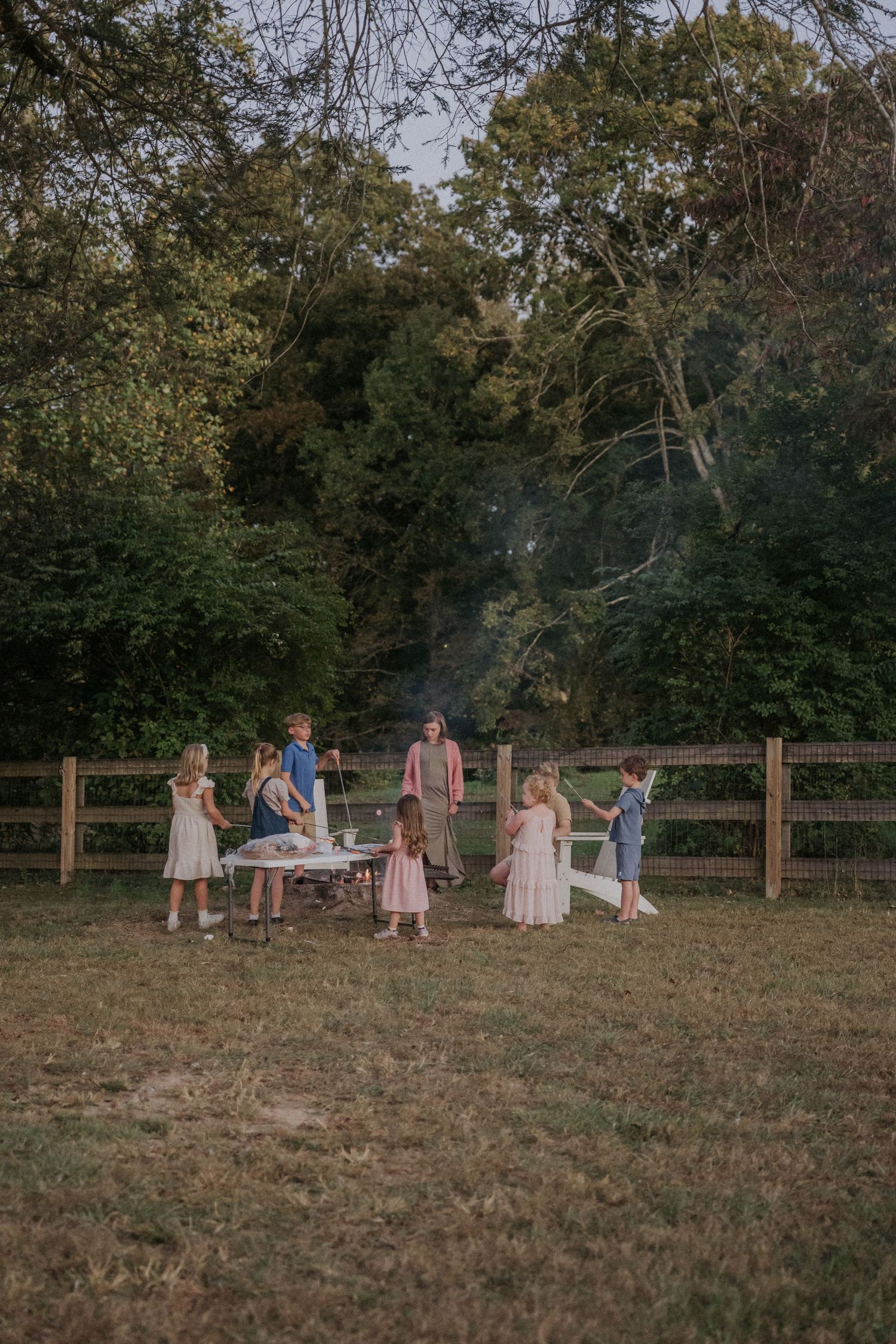 Children playing in a grassy field at sunset with wooden fencing in the background.