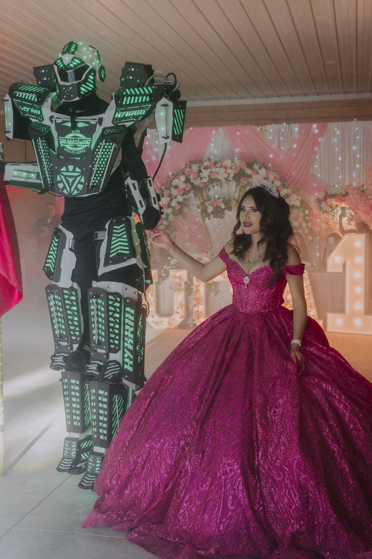 A futuristic LED robot costume poses next to a girl in a flowing magenta ball gown at a Sweet 16 party.