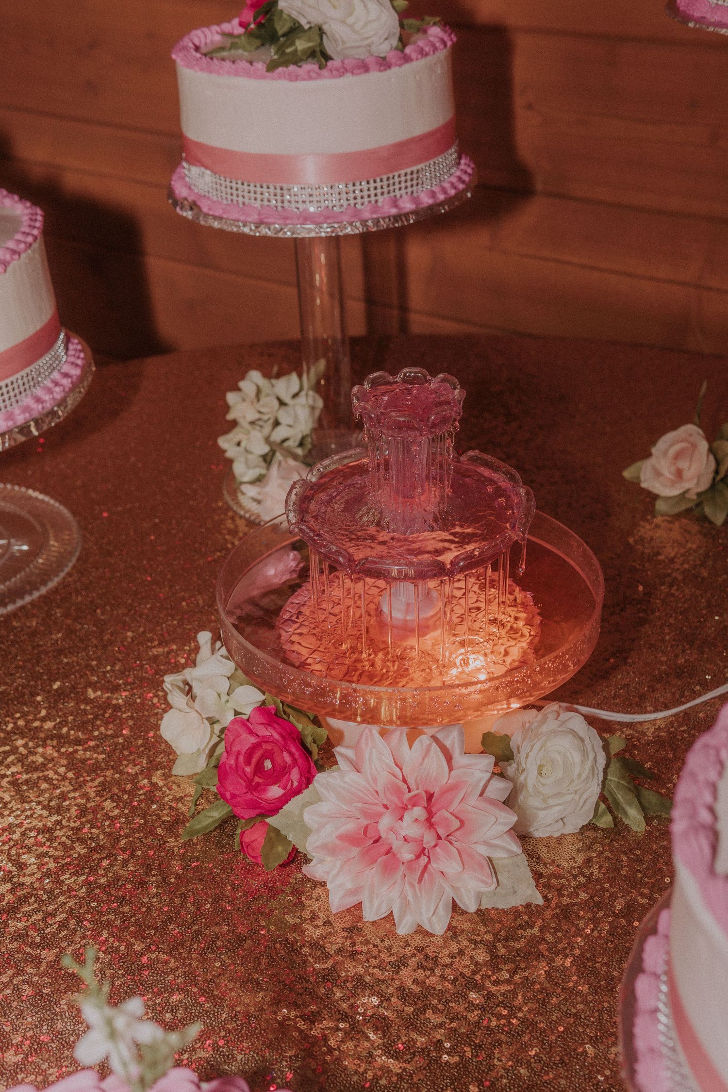Pink and white tiered cake display with floral decorations on rose gold tablecloth.