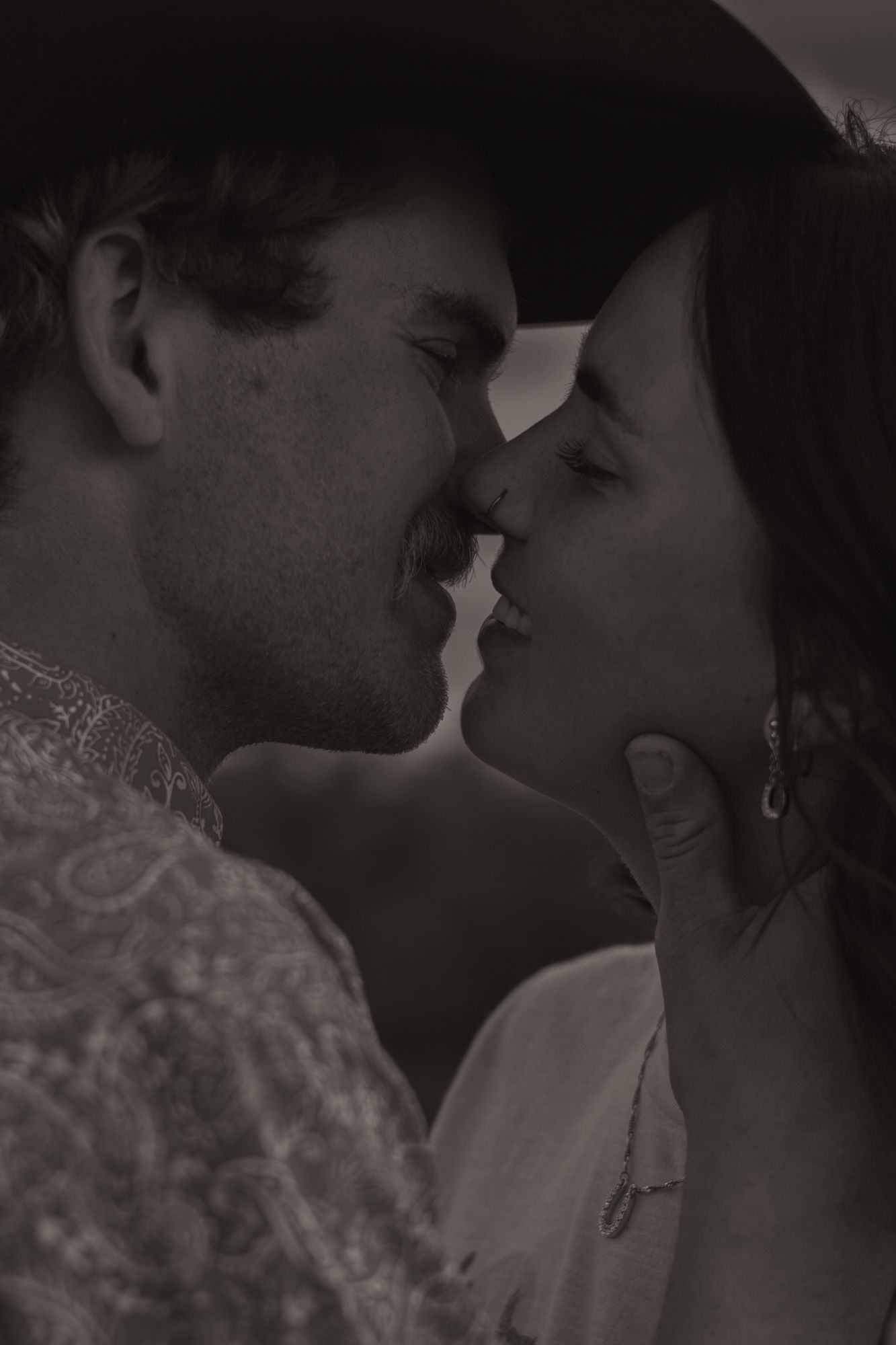 Black and white photo of a couple sharing a romantic kiss, man wearing cowboy hat gently holding womans face.