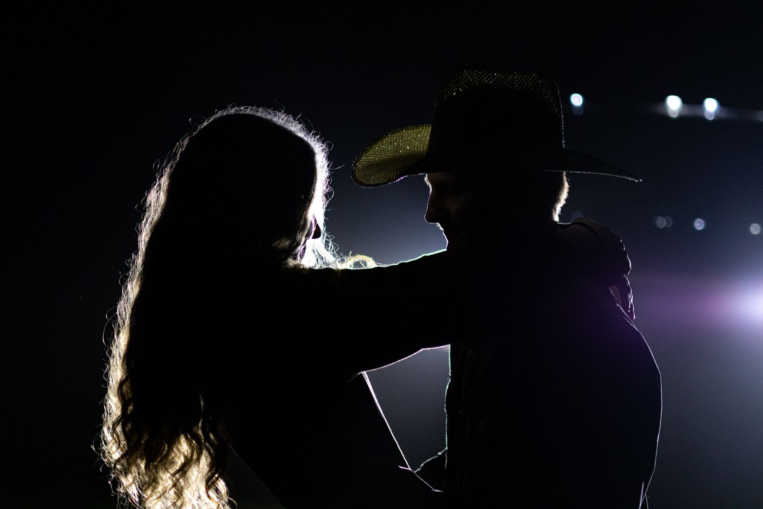 Silhouette of a couple sharing a romantic moment with a cowboy hat against a dark background.