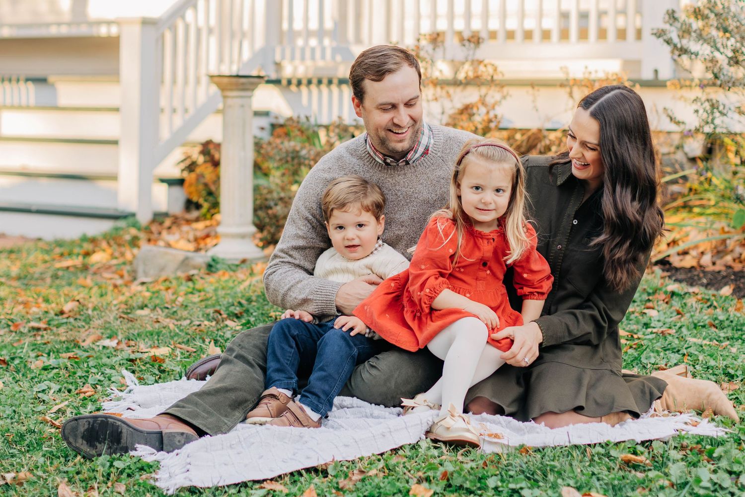 Family enjoys casual outdoor photo session on blanket during fall.