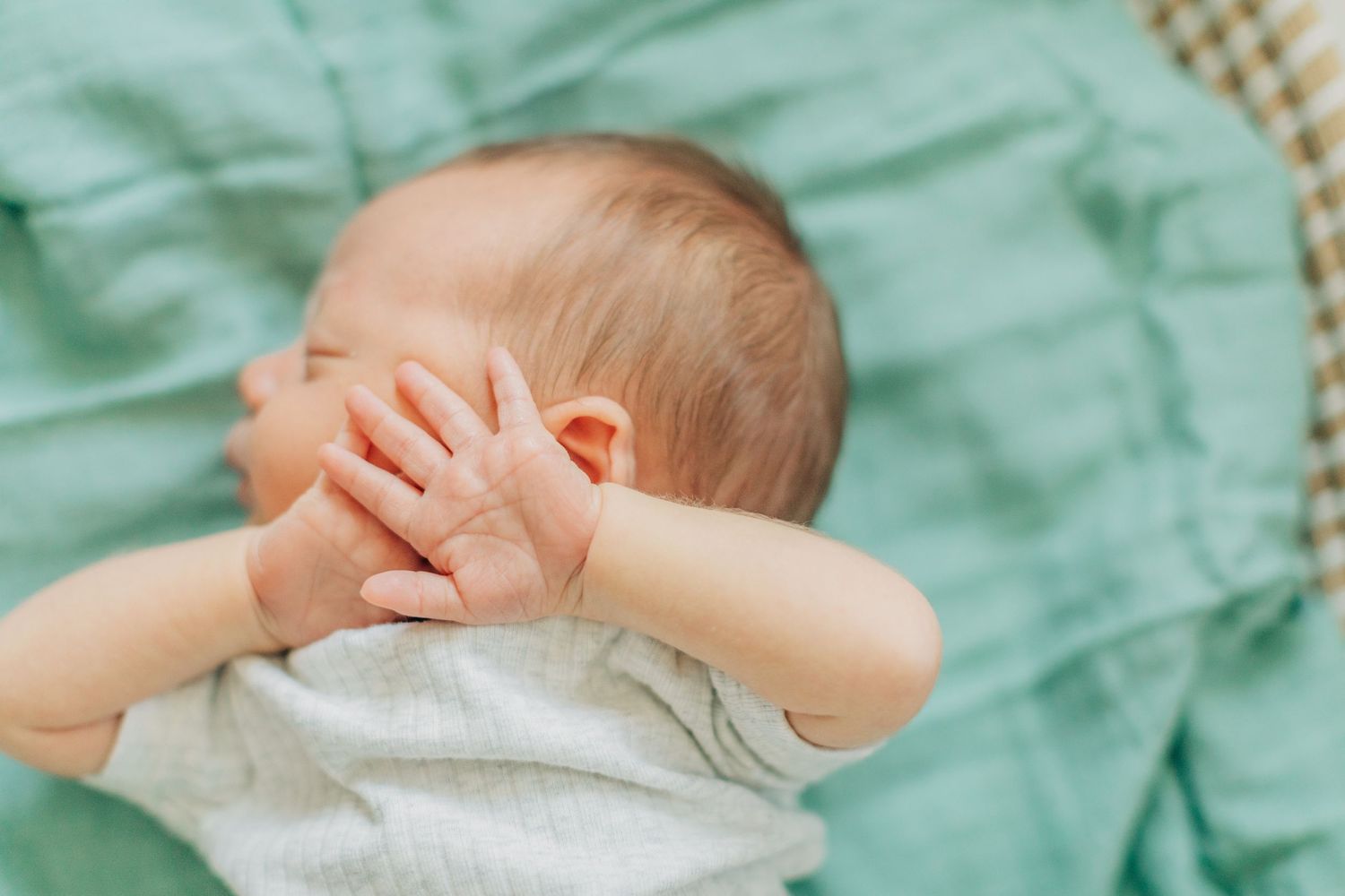 Newborn baby sleeping peacefully on mint green bedding in natural light.