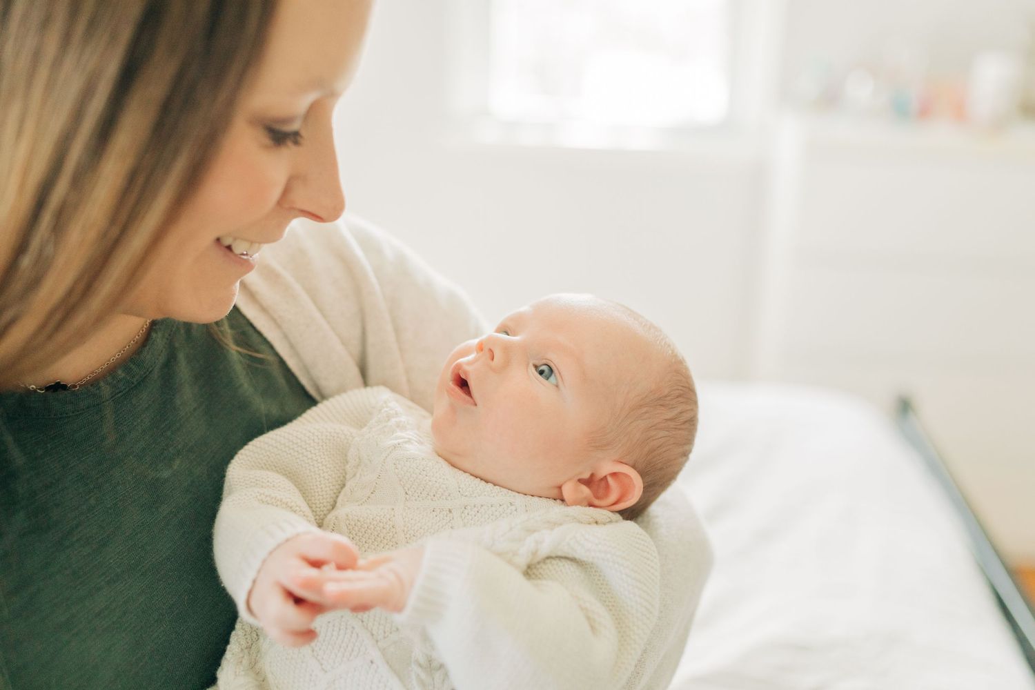 Gentle moment between caregiver and baby in cream outfit against white bedding.