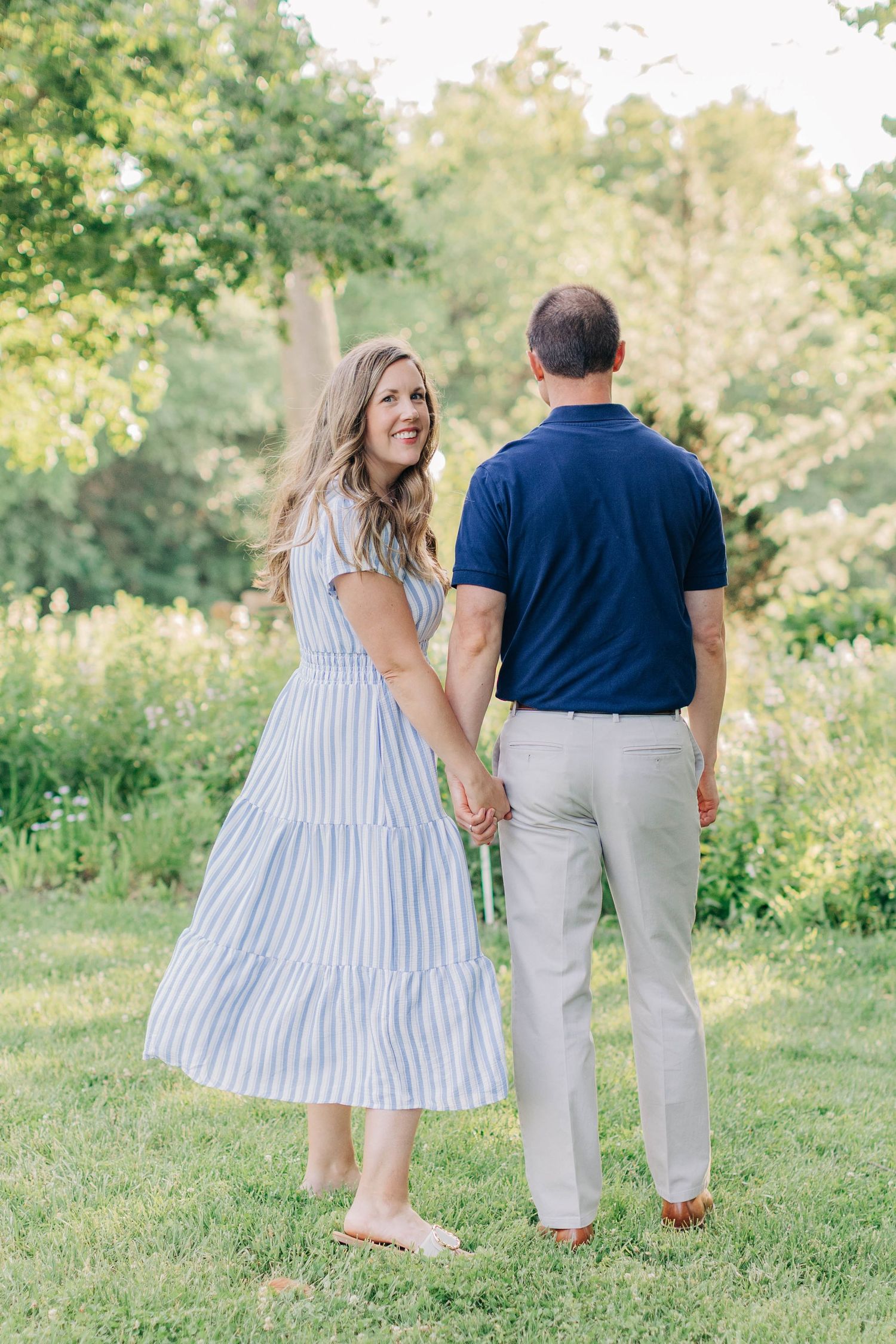 A couple holding hands while walking through a sunny garden landscape.