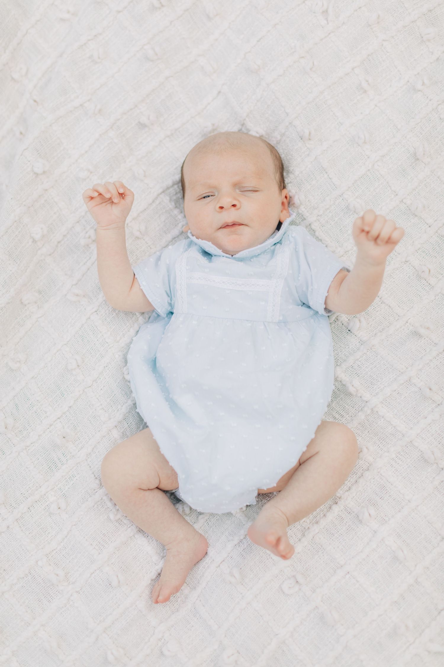 Sleeping infant wearing pale blue clothing on white background.
