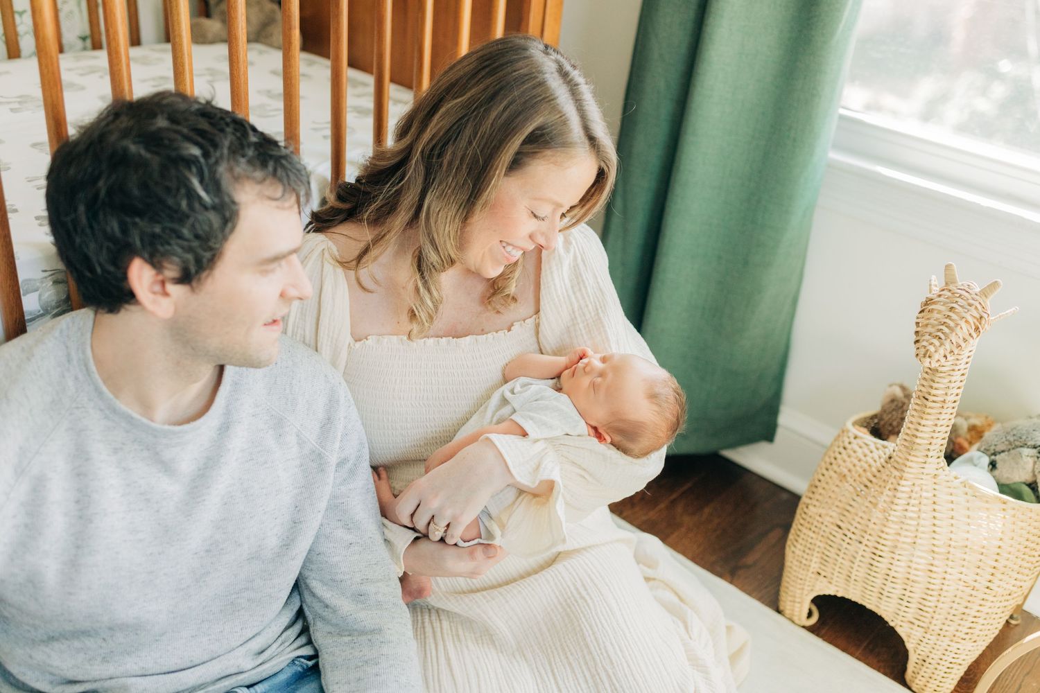 Intimate family portrait in front of wooden crib and green curtains.