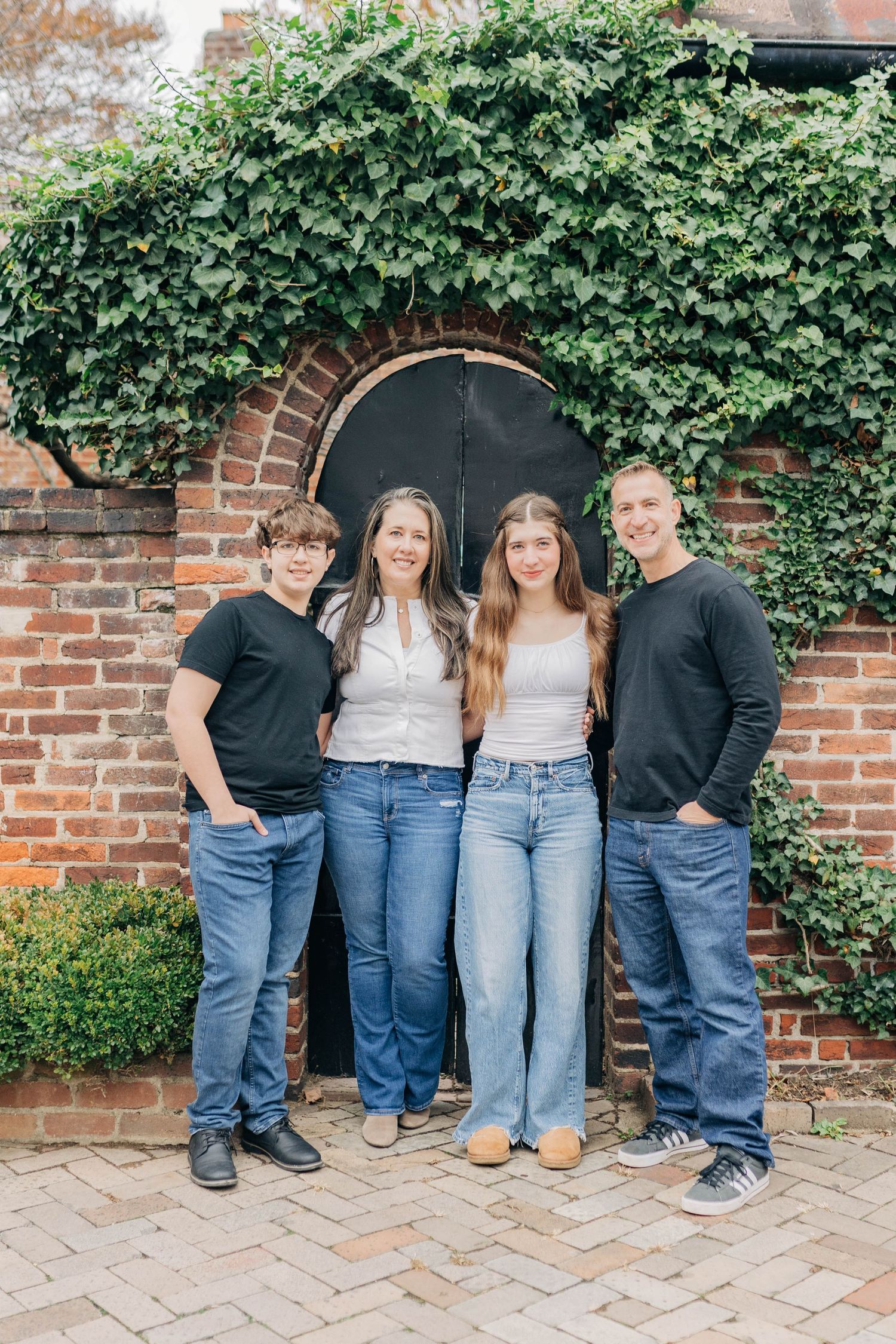 A group photo of four people in casual attire standing in front of an ivy-covered brick wall.