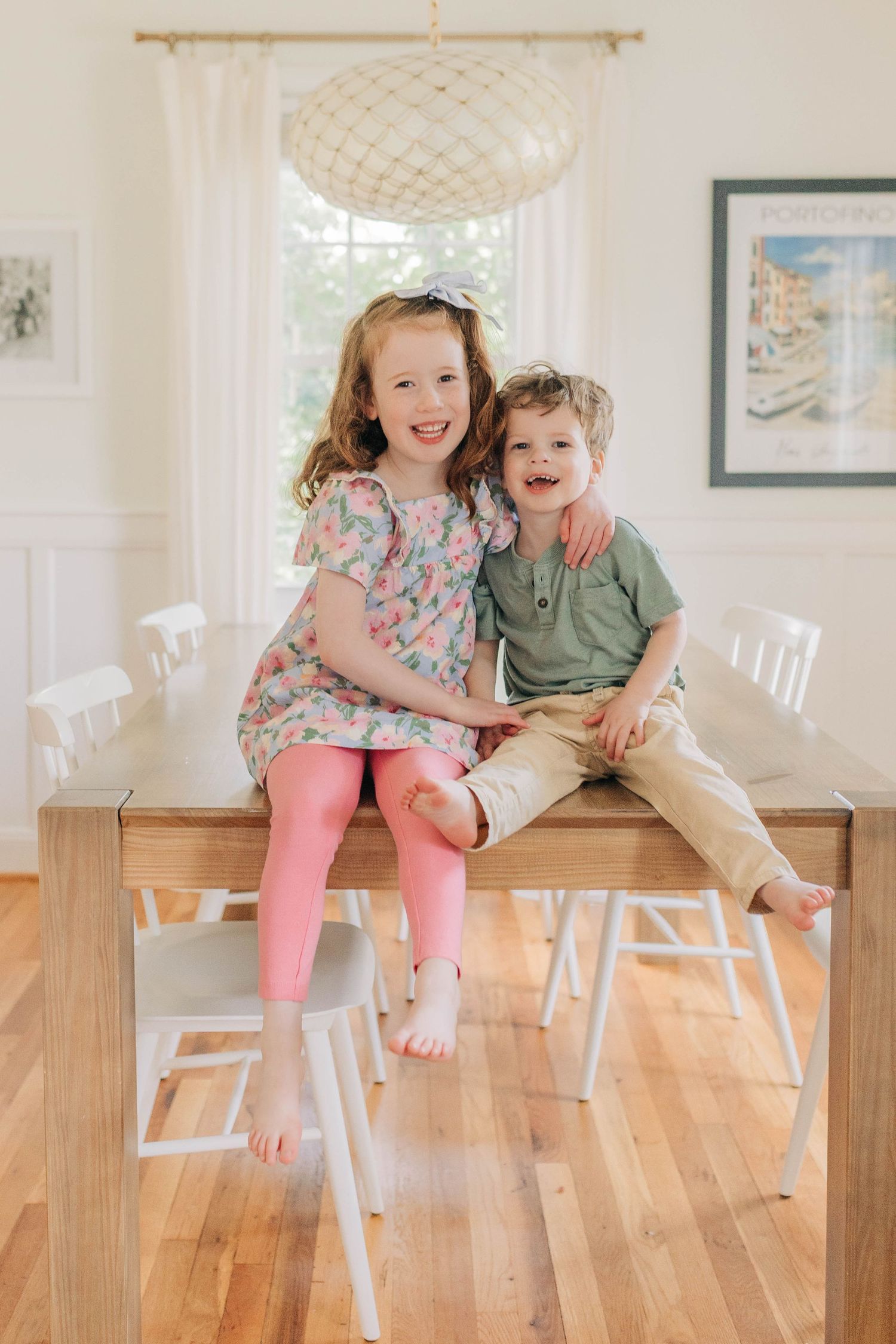 Children sitting together on a wooden bench in a sunny white room.