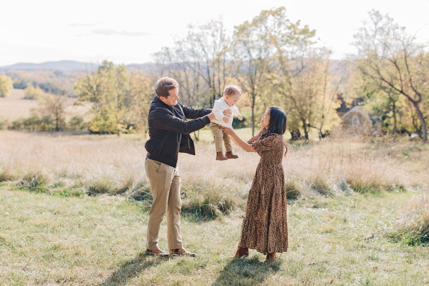 A family plays together in an open field with rolling hills in the background.