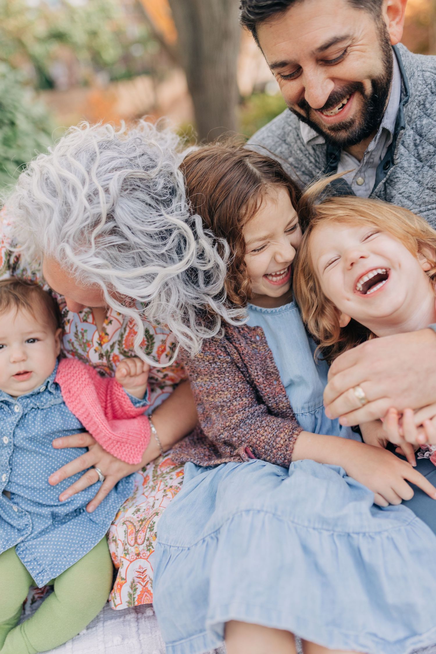 A joyful multigenerational family laughing and hugging outdoors, with grandma, dad, and three young girls sharing a warm moment.