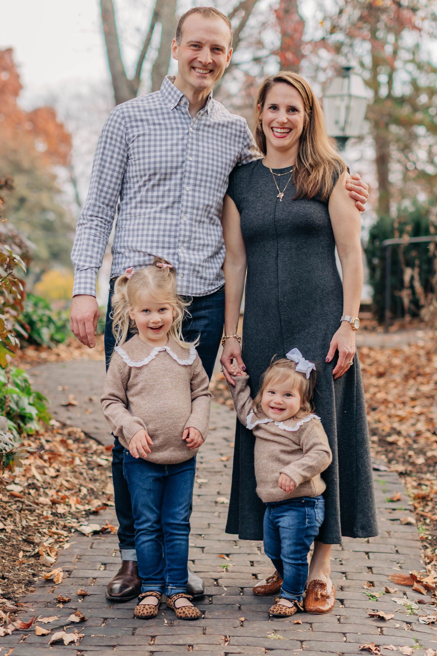 Family of four posing on a brick path surrounded by autumn foliage.
