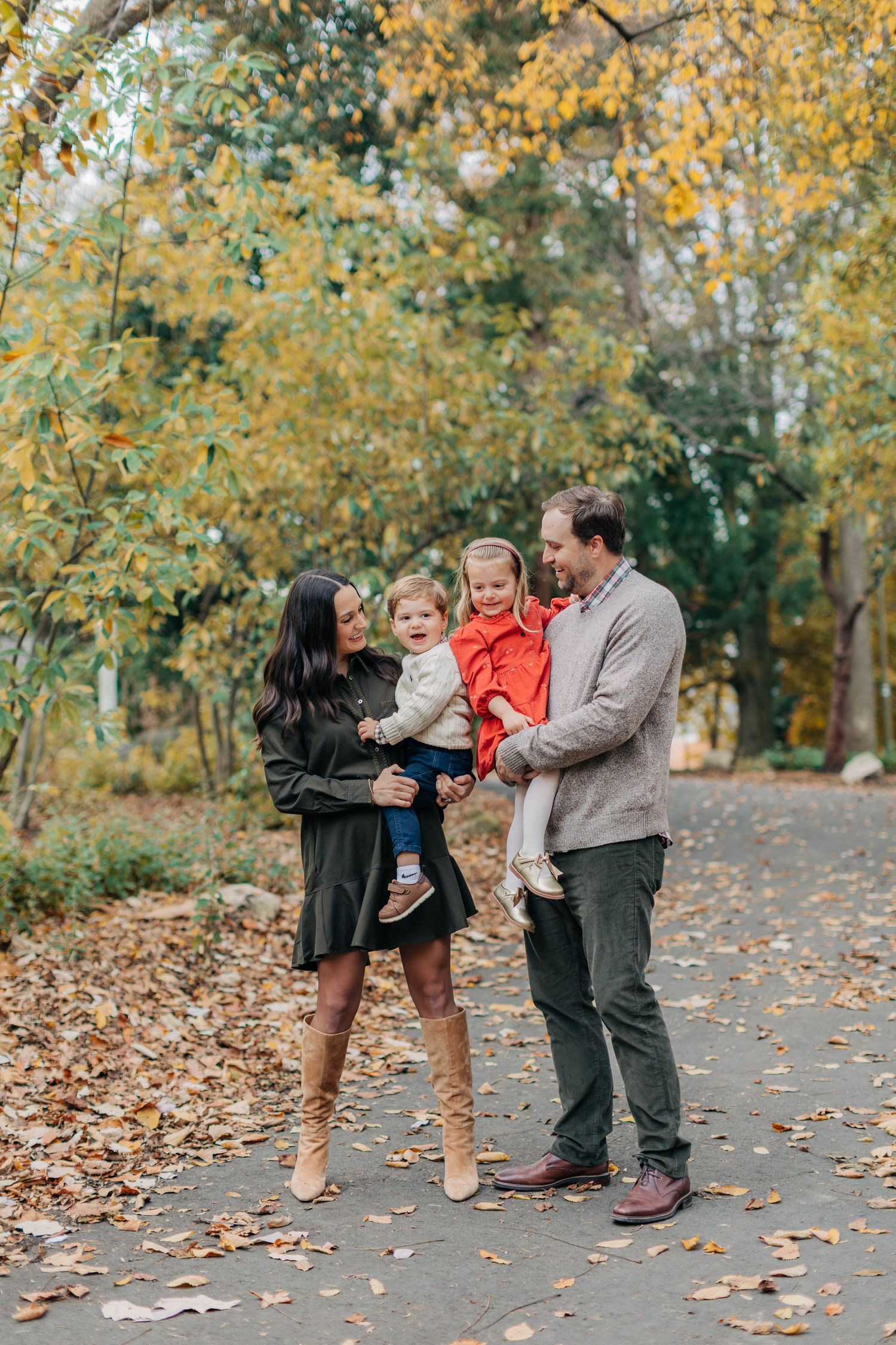 Family shares playful moments together on autumn path covered in fallen leaves.