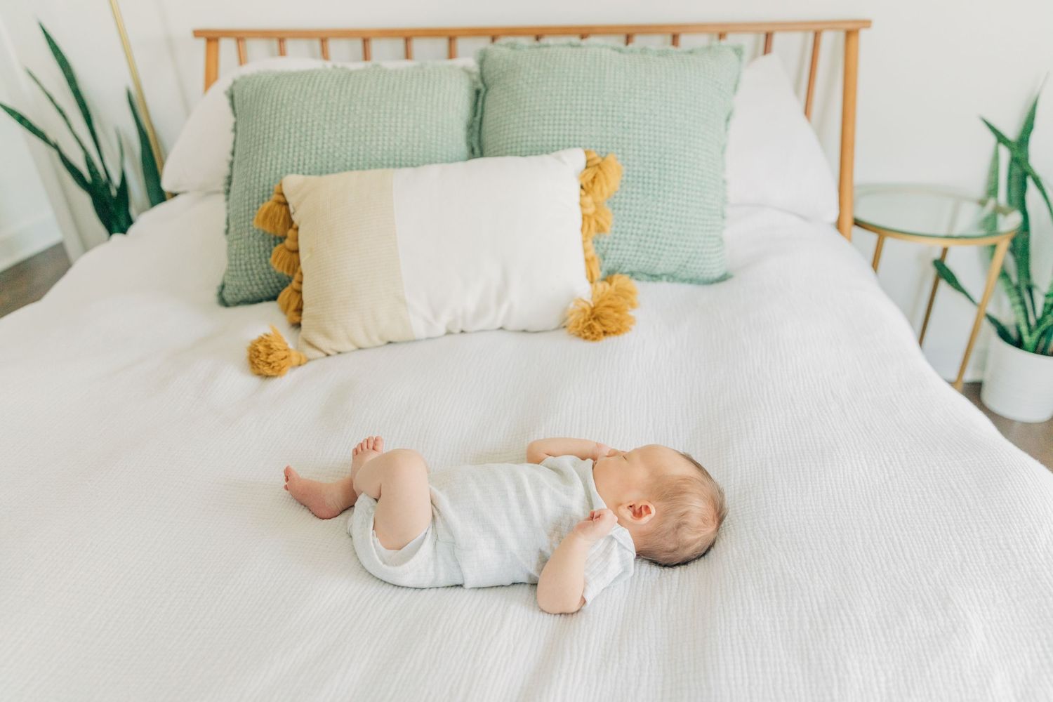 Newborn baby sleeping on white bedding with mint green accents and wooden headboard.