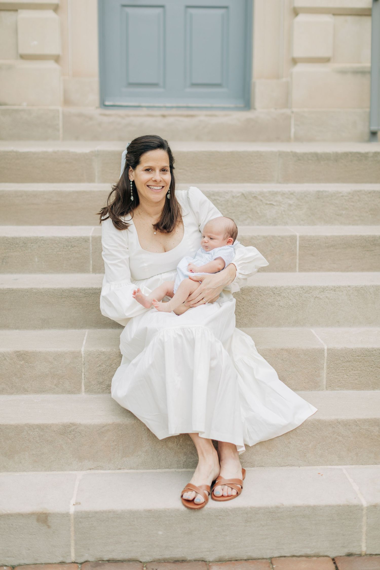 Elegant portraits on stone steps featuring white dress and newborn baby in natural light.