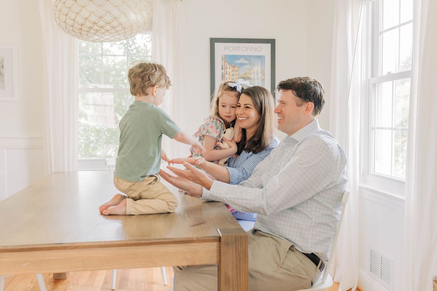 Happy family gathering around a wooden dining table in a sunlit room.
