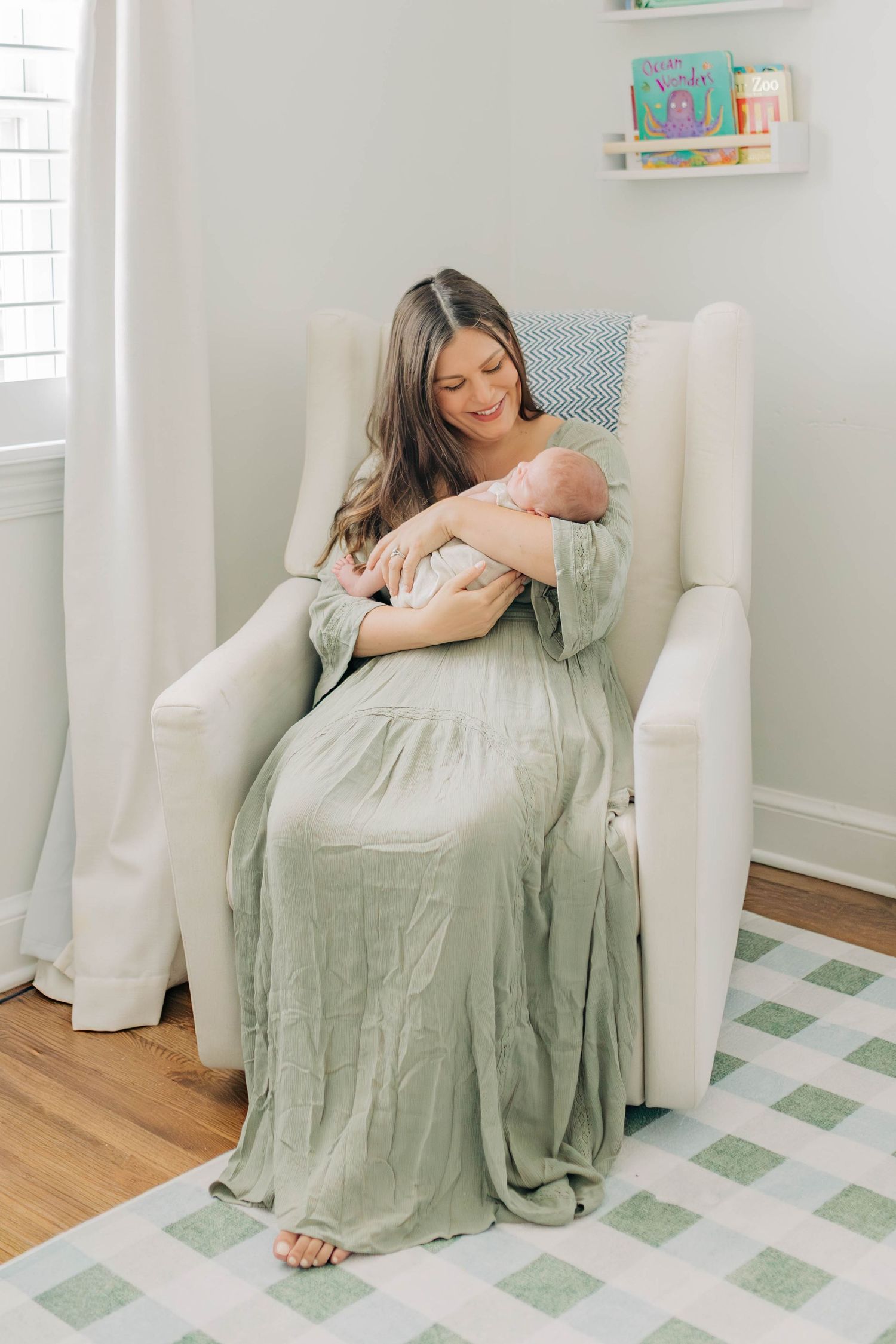 A mother in sage green dress relaxes with her children in a bright nursery room.