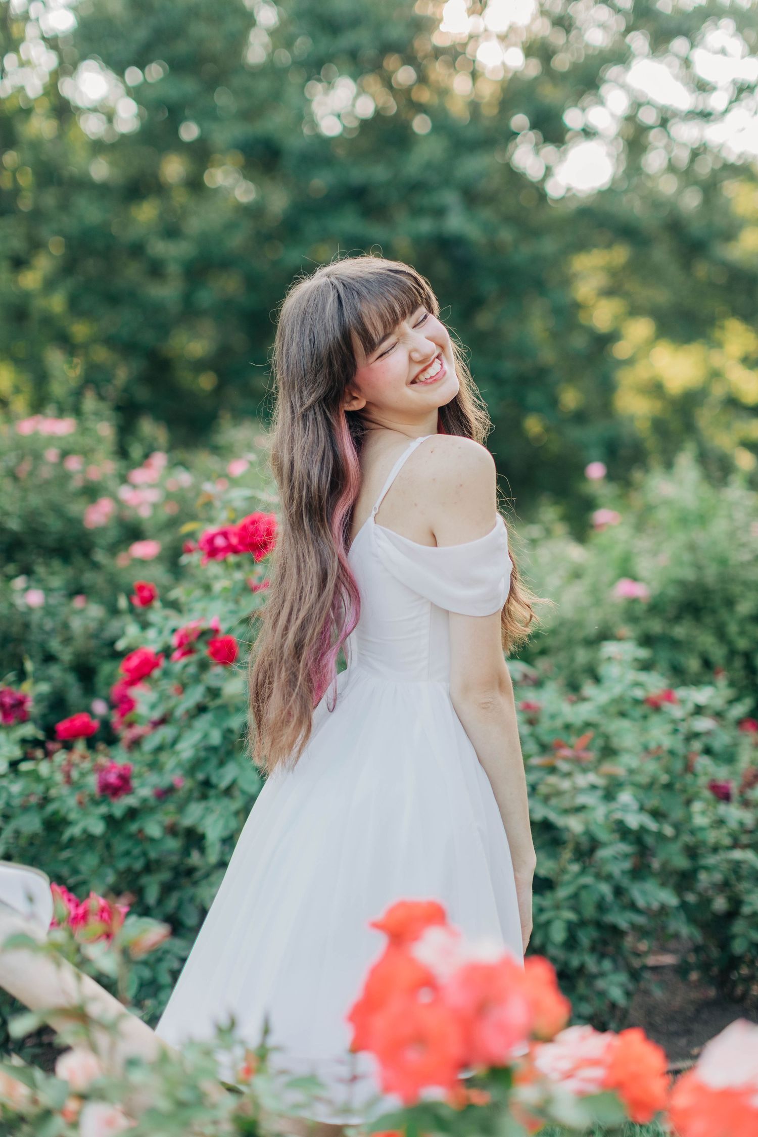 Playful summer portrait amidst vibrant red and coral roses in a sunlit garden setting.