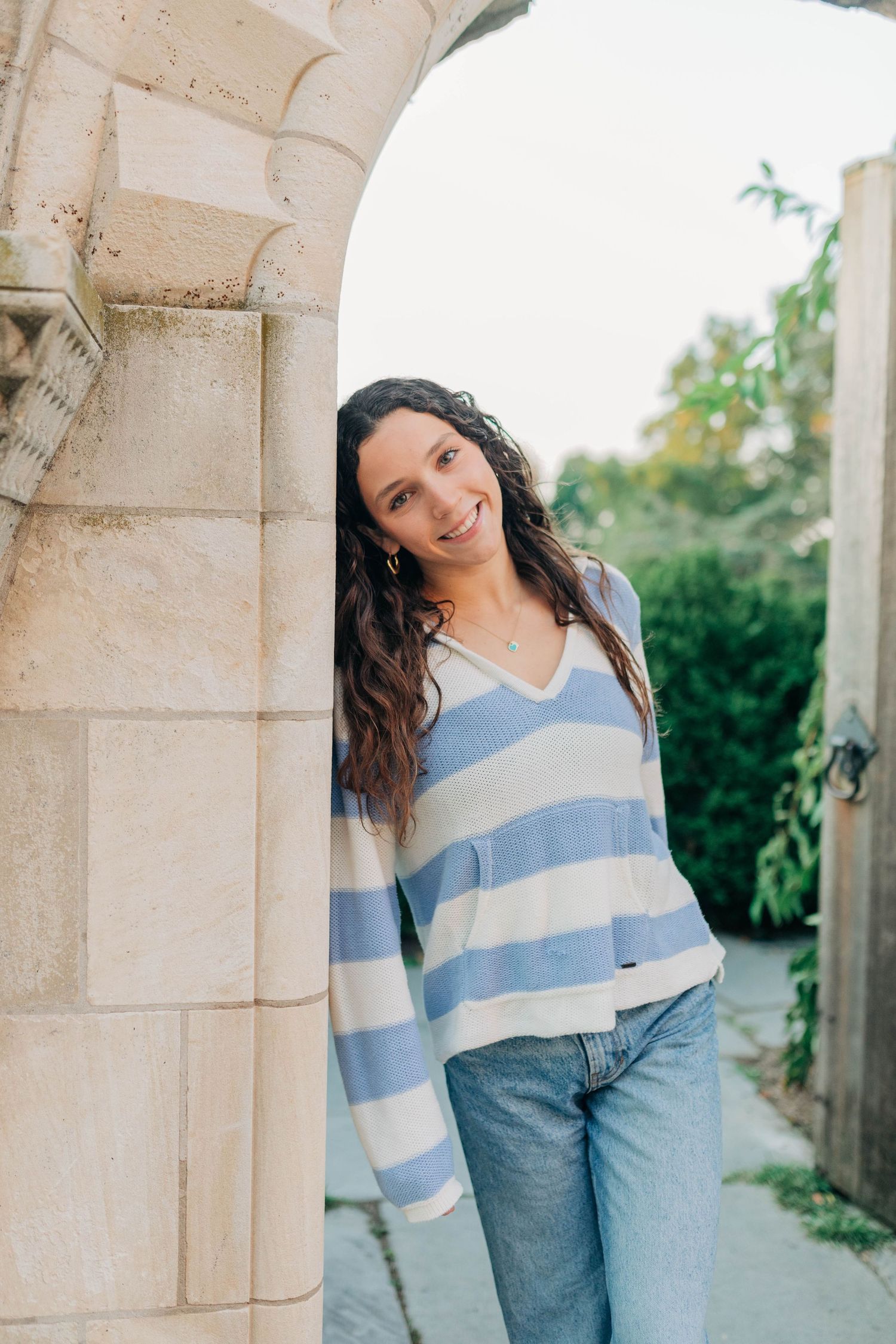 A casual portrait against stone archways wearing a blue striped sweater and jeans.