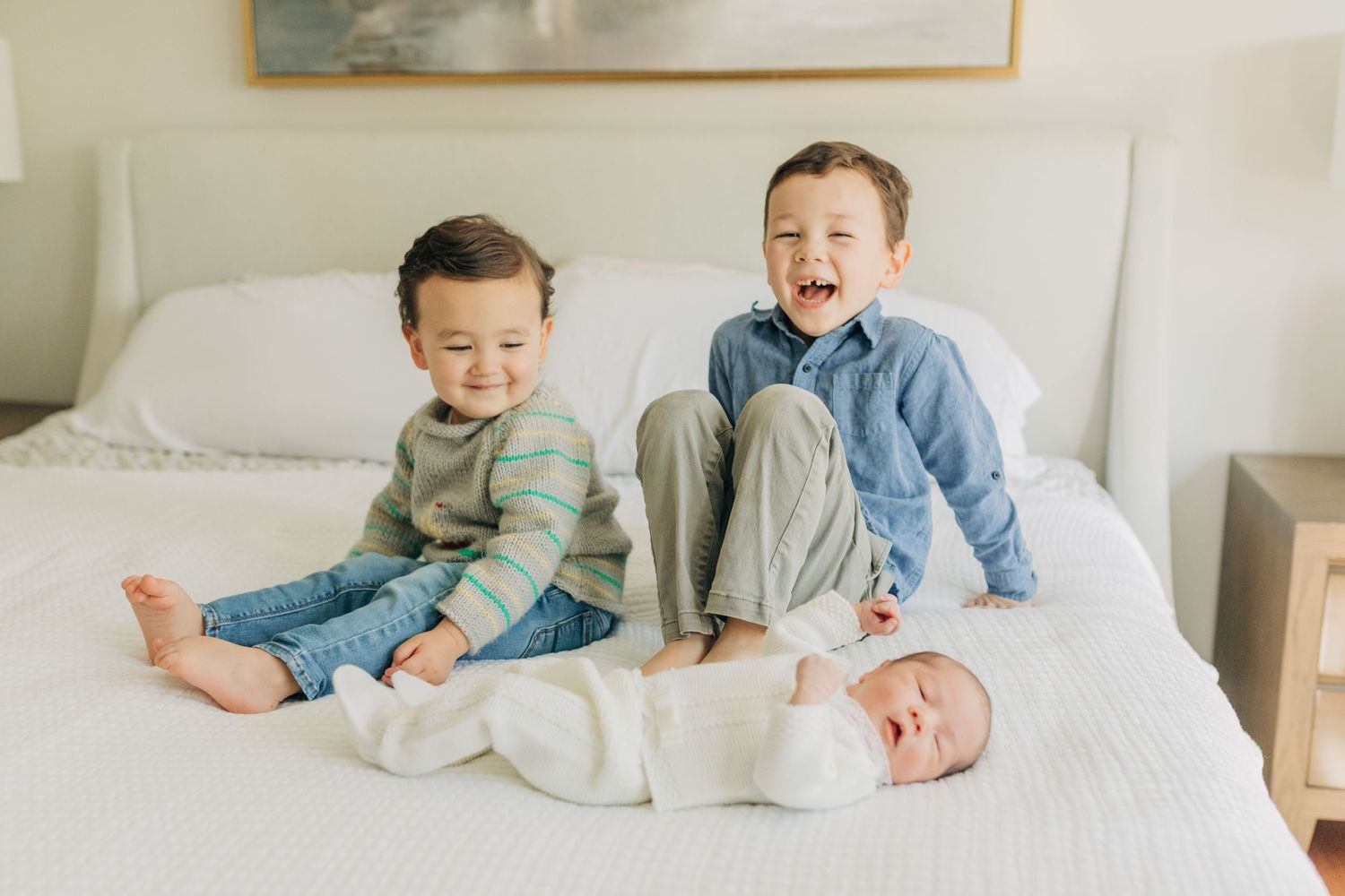 Three young children share sweet moments together on a cozy white bed.