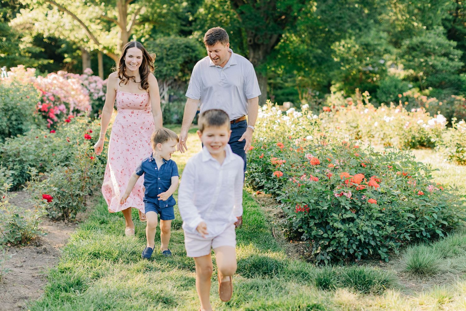 Happy family of four walking through a lush garden path, two boys running ahead of their smiling parents.
