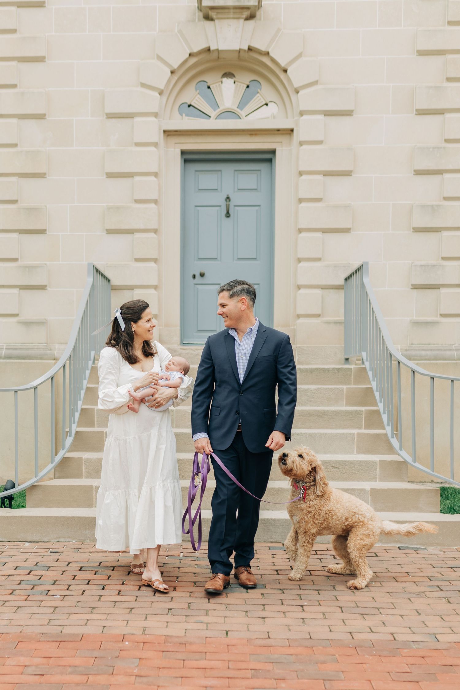 Family portrait with goldendoodle dog on brick patio in front of stone building.