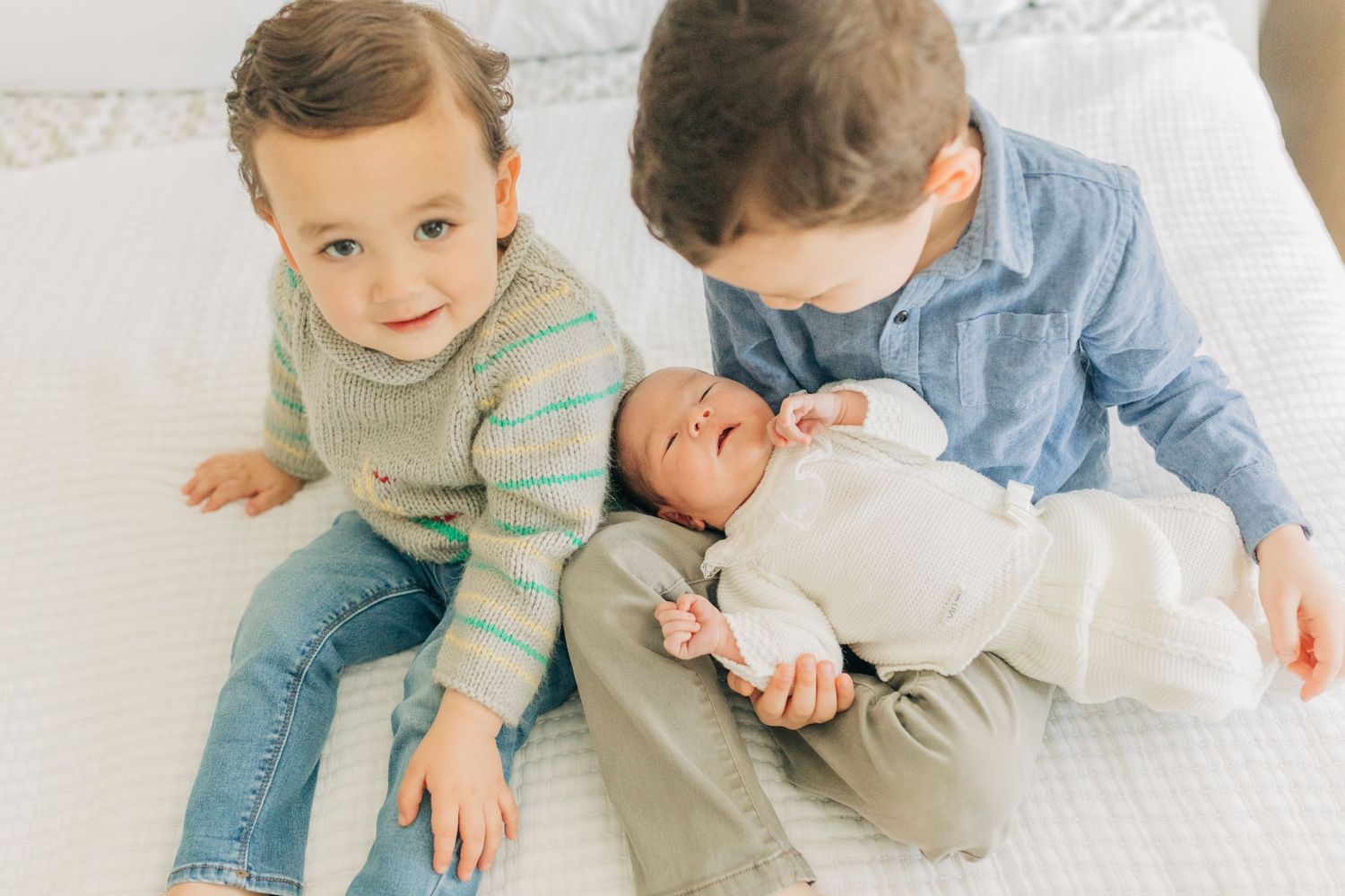 Siblings share tender moments together on white bedding in natural light.