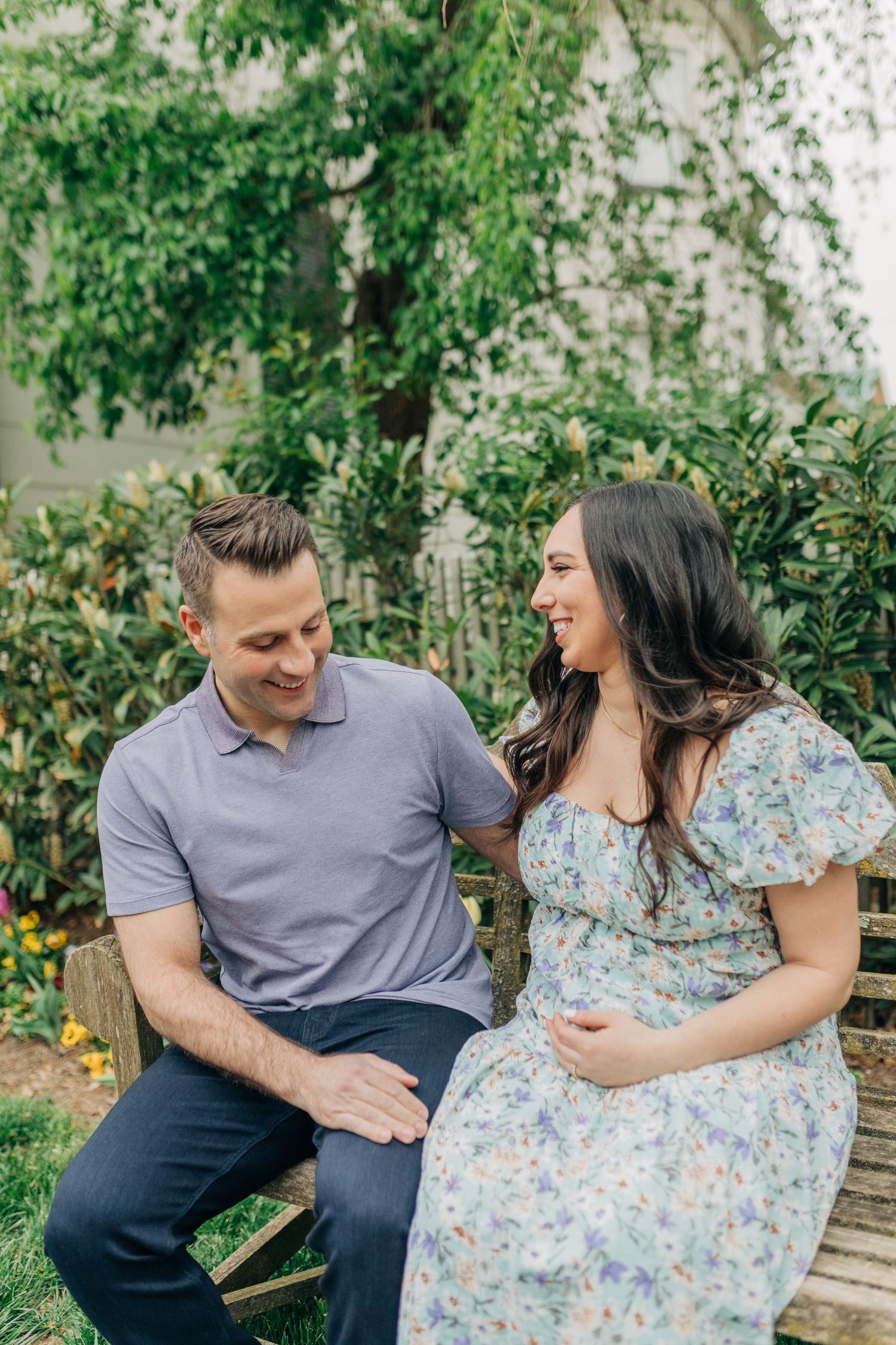 A couple shares candid laughing moments together on a garden bench.