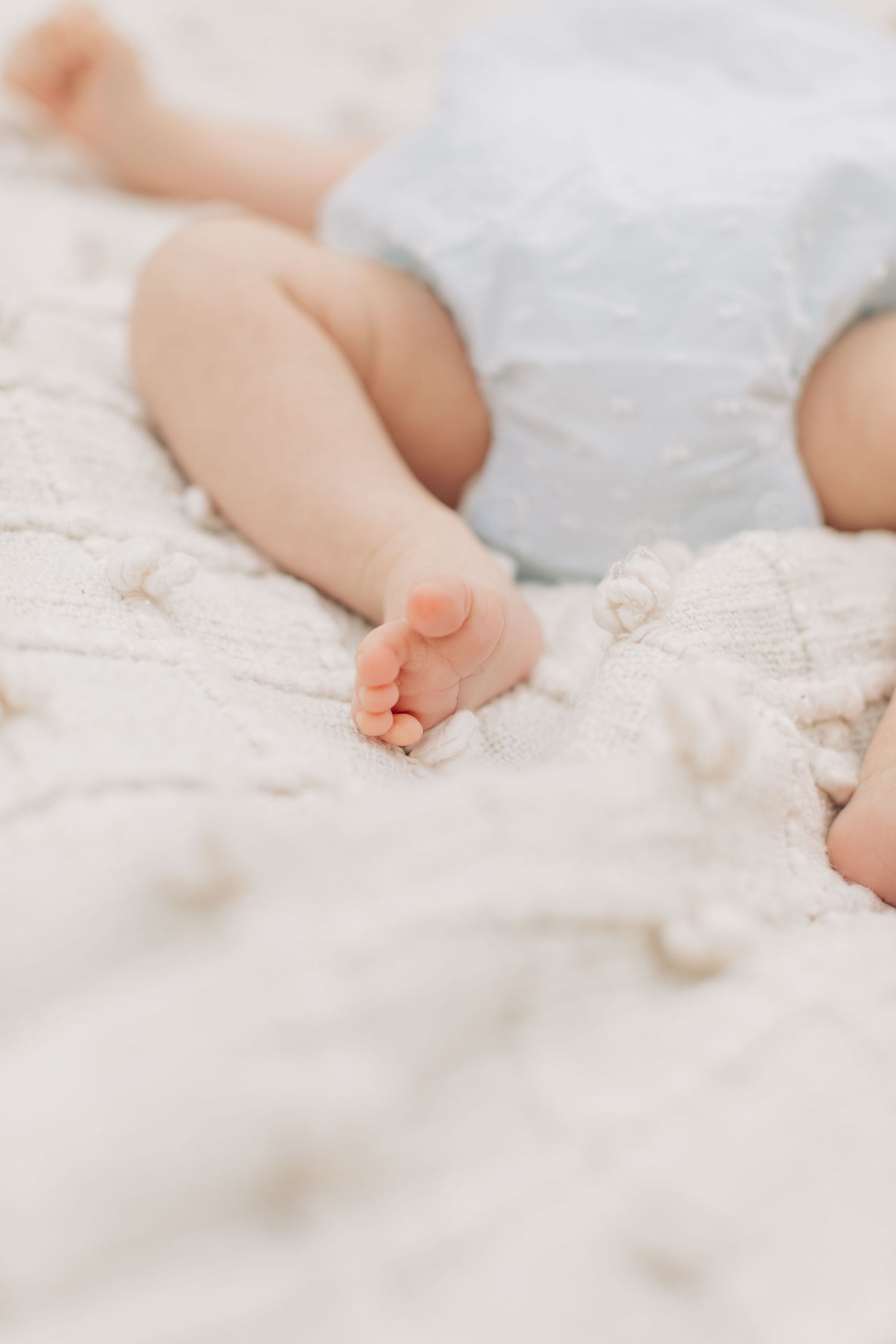 Close-up of baby feet resting on soft white textured blanket.
