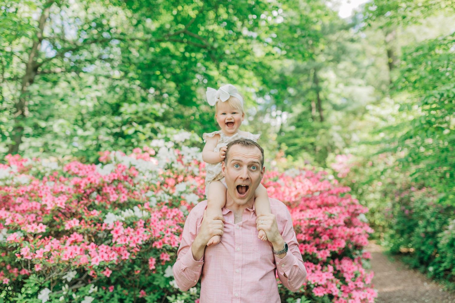 Joyful outdoor portrait in front of vibrant pink azalea bushes in a garden setting.