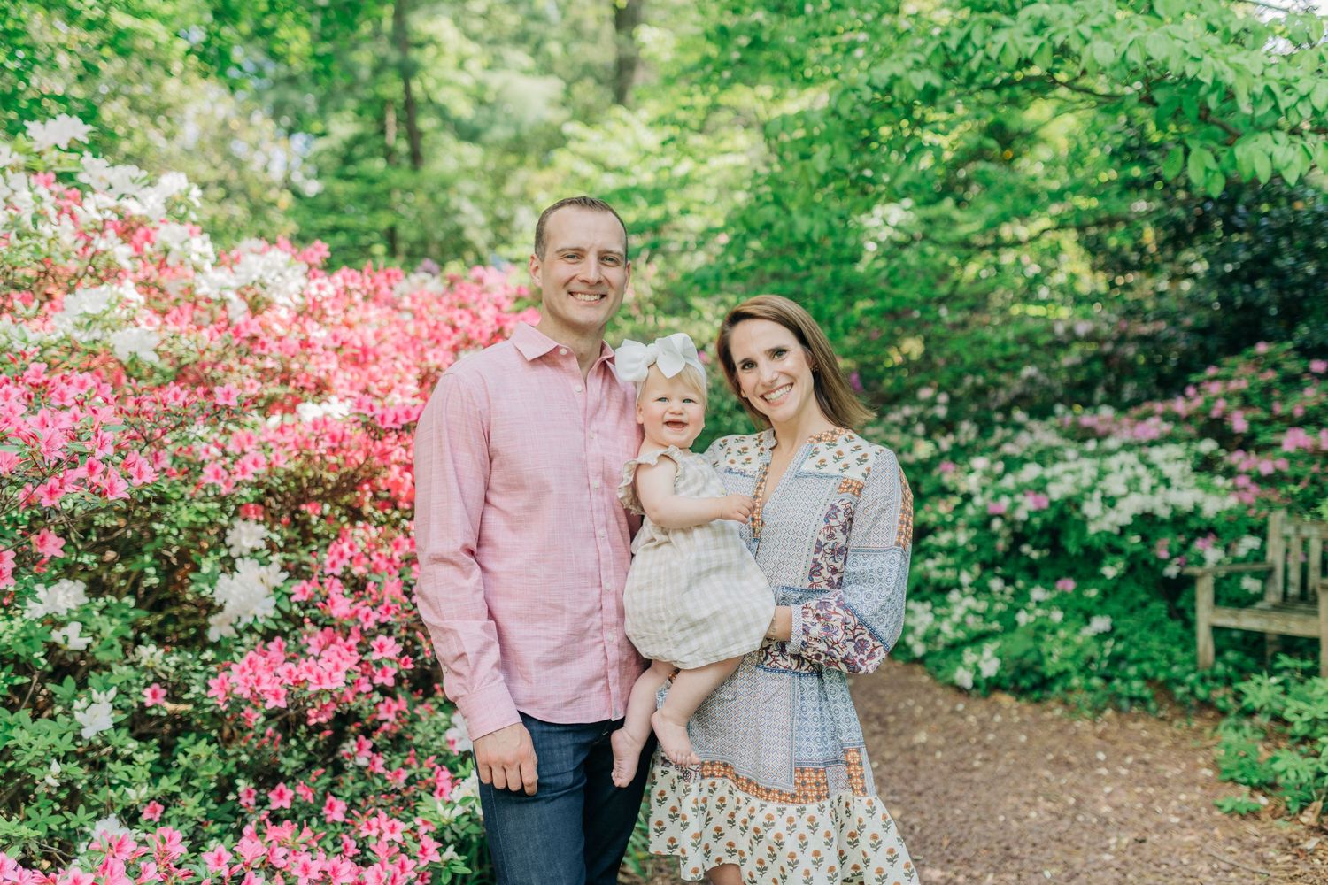 Family photo session in lush green garden with pink flowering trees.