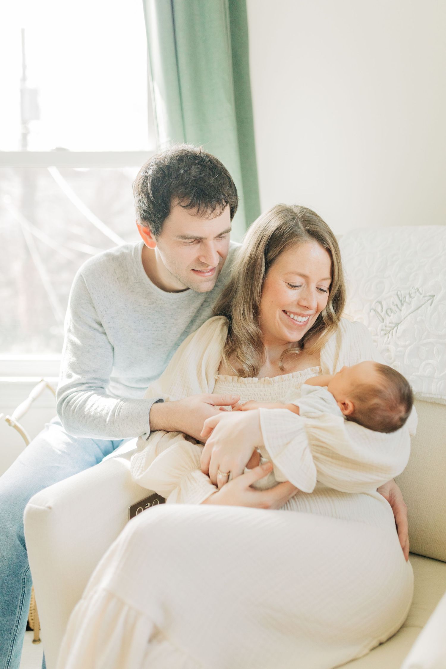 Tender family moment in sunlit living room with white furnishings.